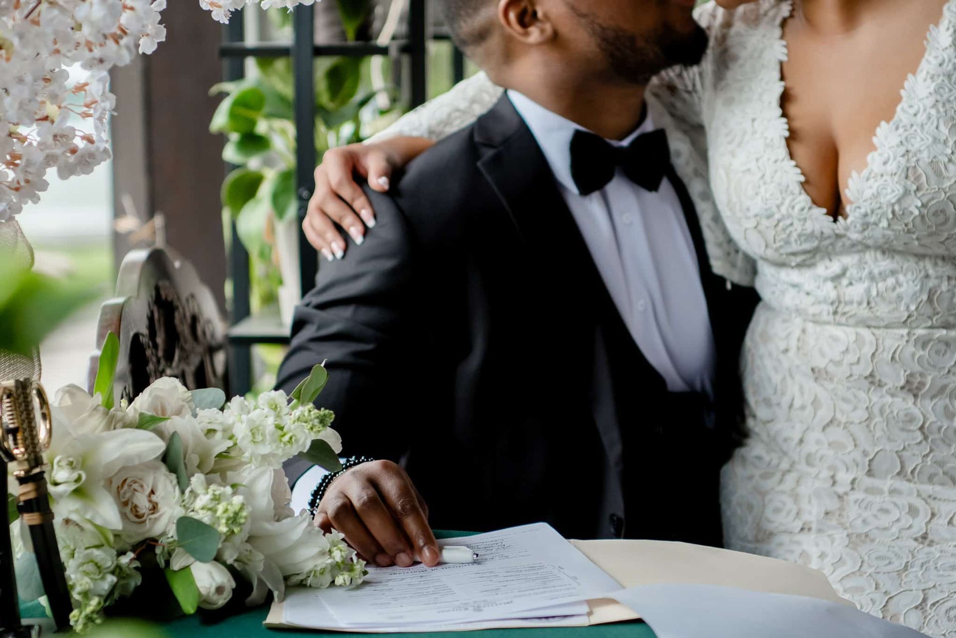 A bride and groom are kissing while signing a wedding contract.