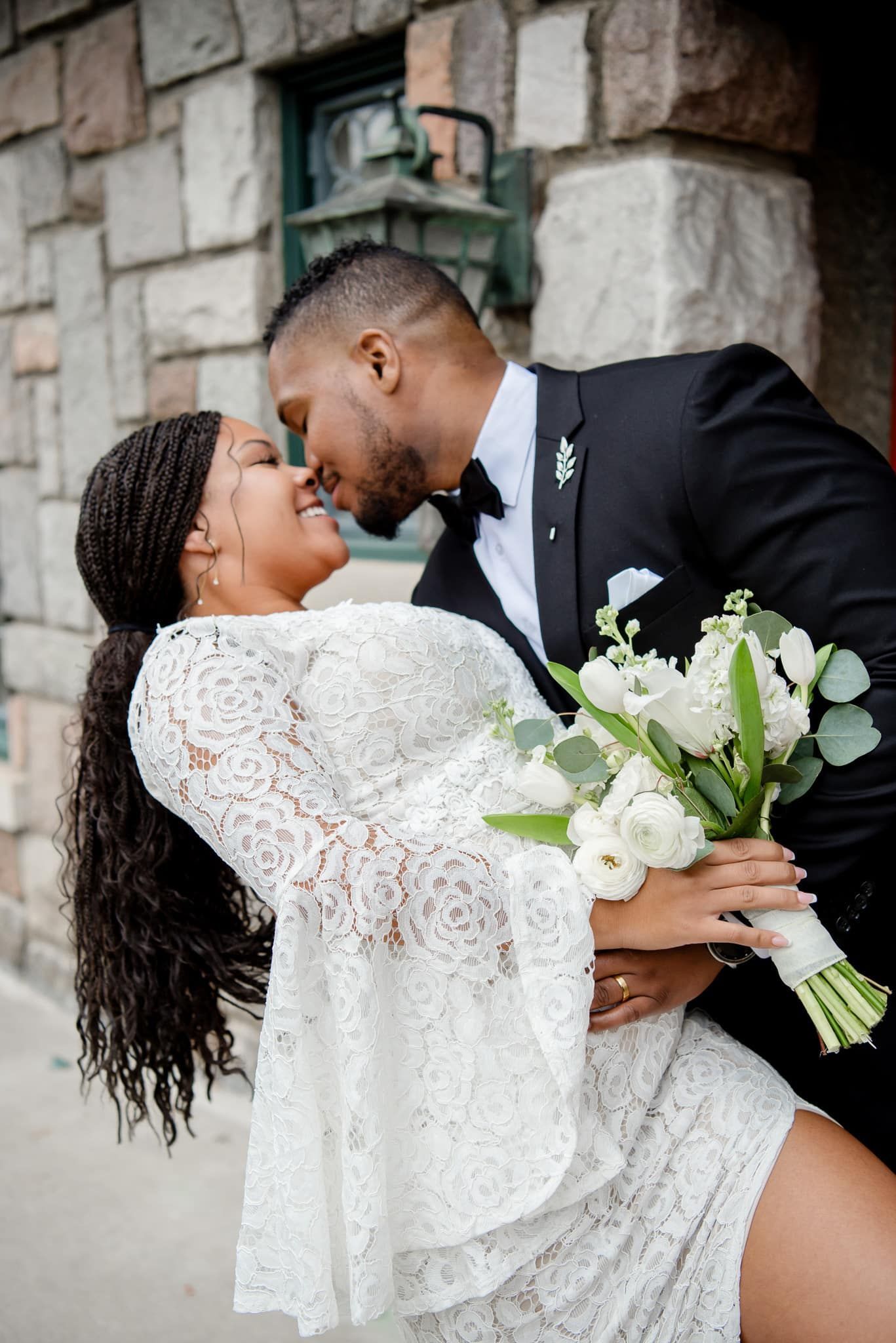 A bride and groom are kissing while the bride is holding a bouquet of flowers.