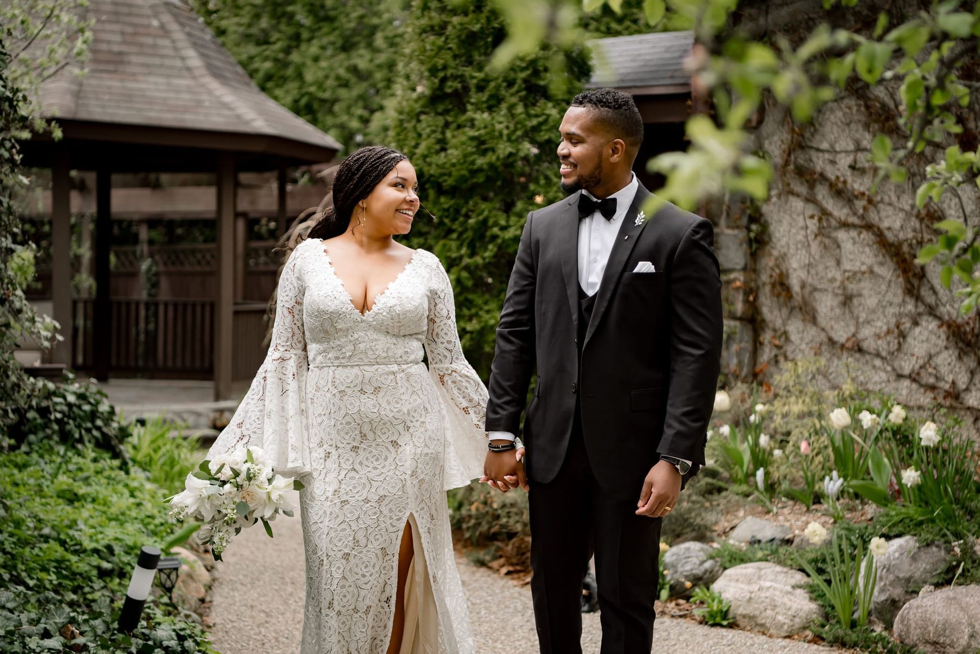 A bride and groom are holding hands while walking in a garden.