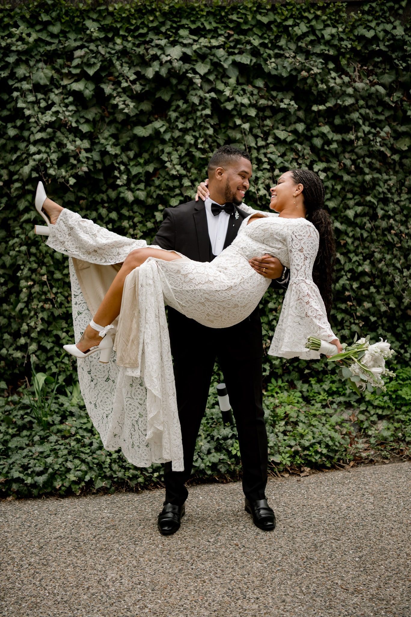 A bride and groom are posing for a picture and the groom is holding the bride in his arms.