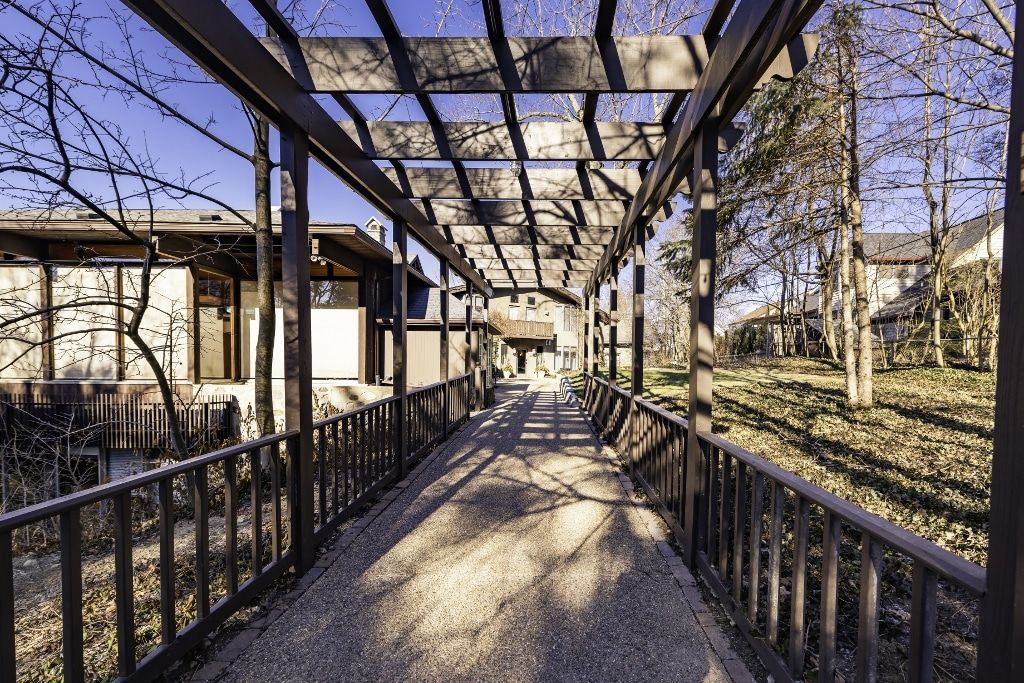 A long walkway leading to a house with a pergola over it.