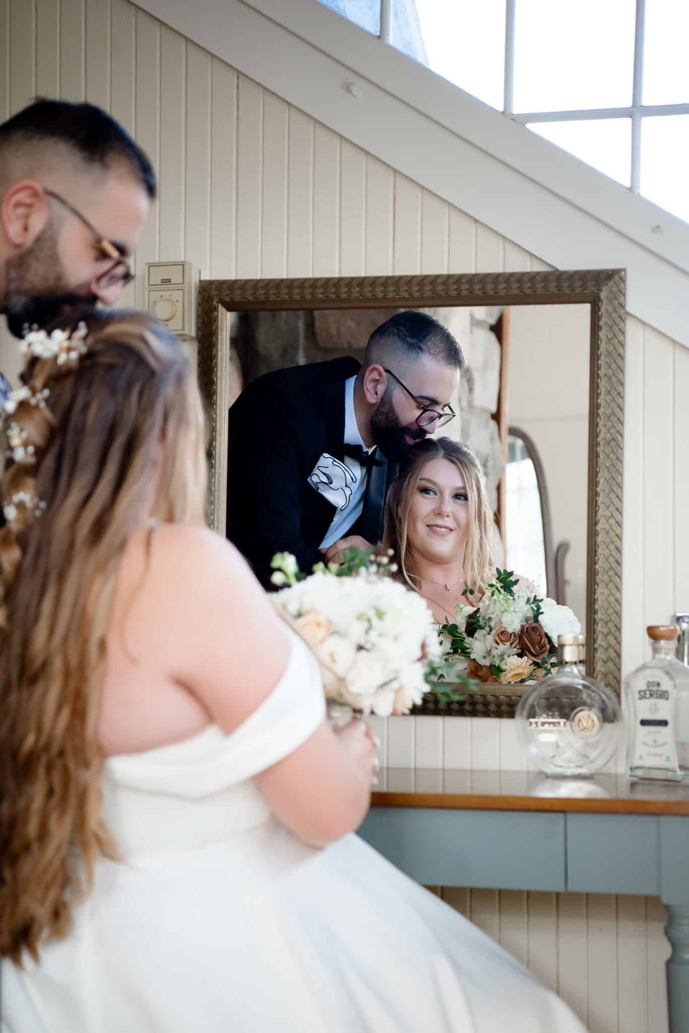 A bride and groom are looking at their reflection in a mirror.