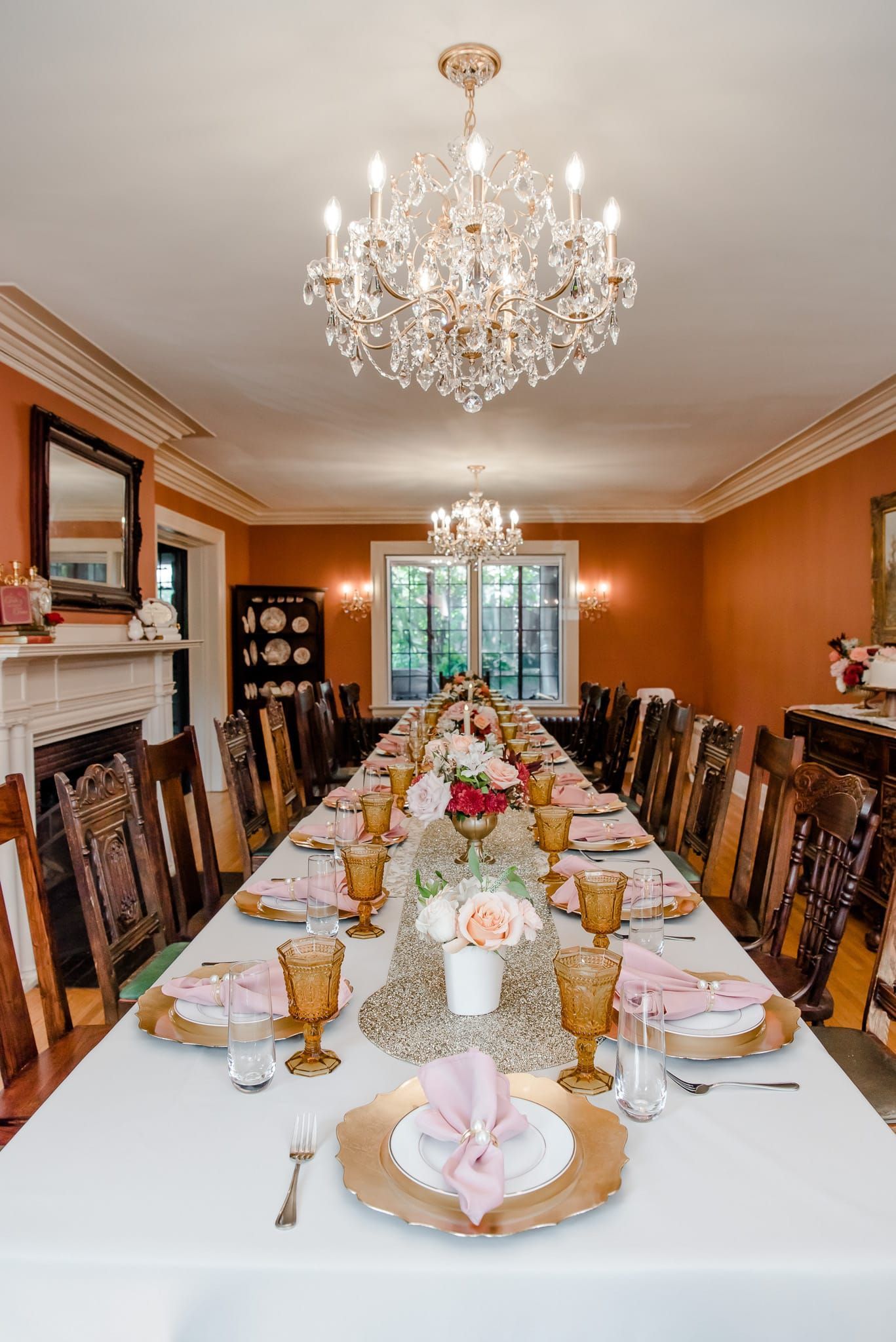 A long table is set for a dinner party in a dining room with a chandelier.