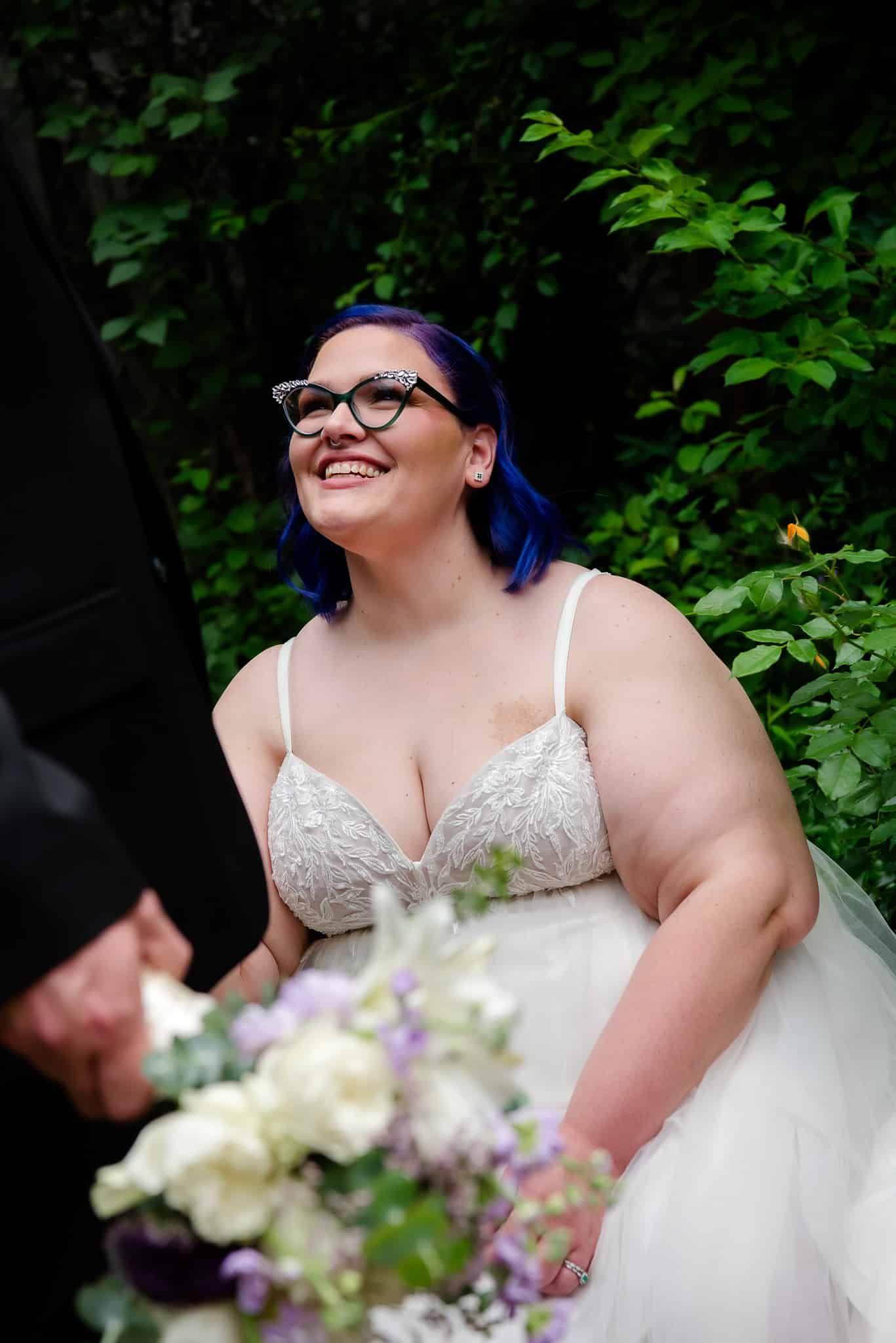 The bride is wearing glasses and holding a bouquet of flowers.