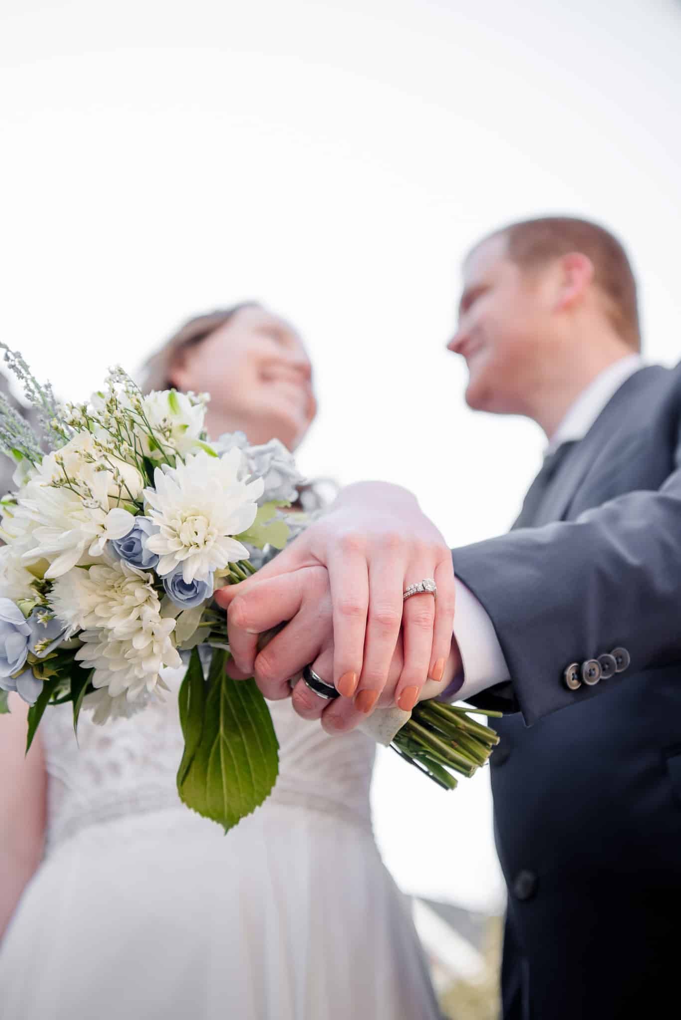 A bride and groom are holding hands and the bride is holding a bouquet of flowers.