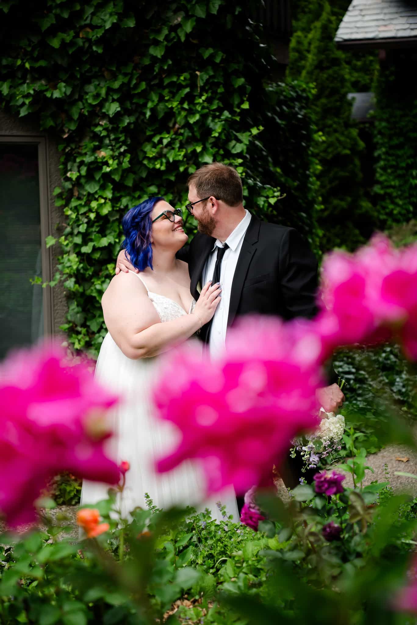 A bride and groom are posing for a picture in a garden surrounded by pink flowers.
