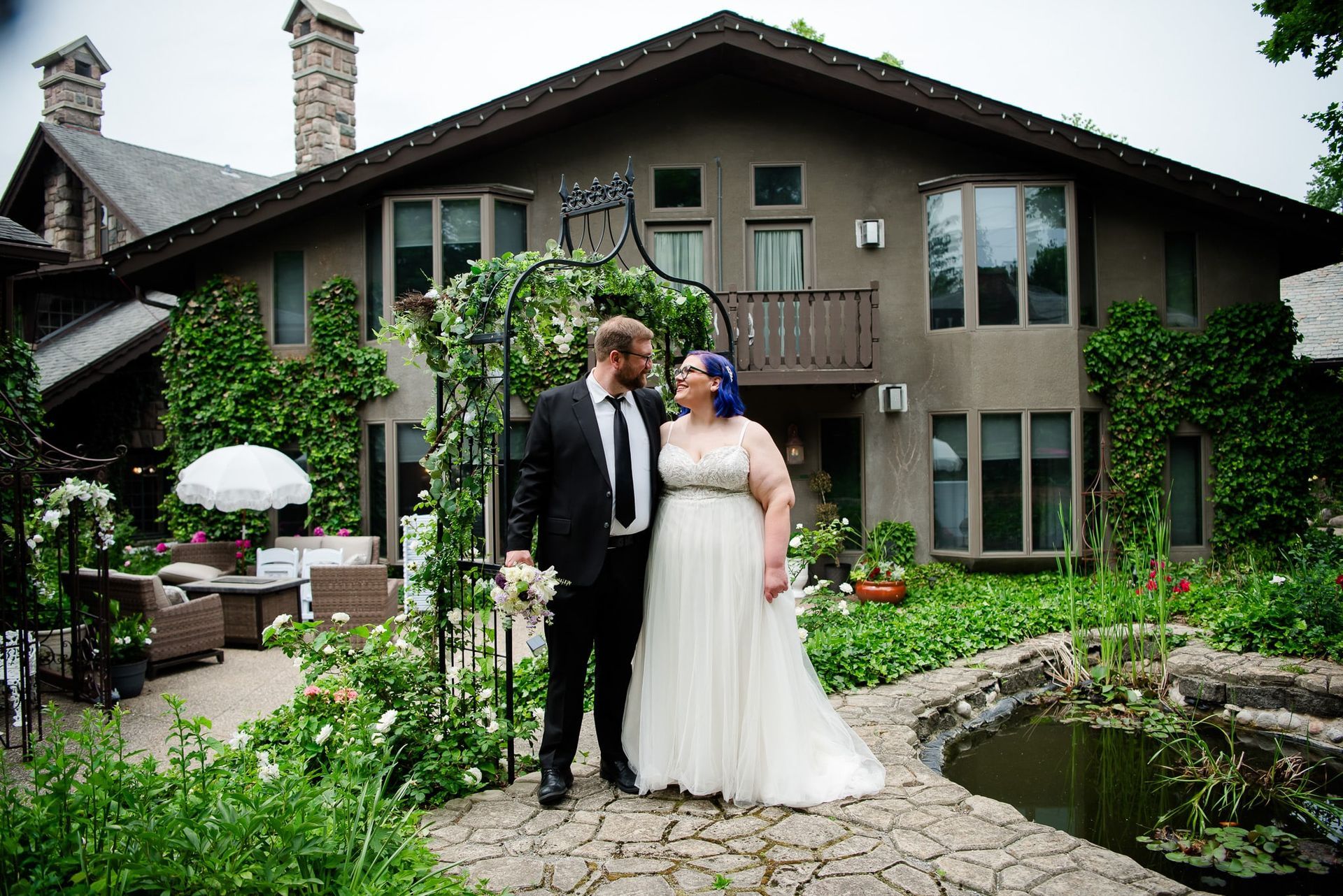 A bride and groom are posing for a picture in front of a large house.