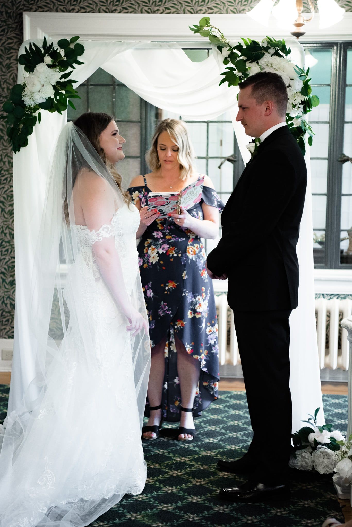 A bride and groom are standing under an arch during their wedding ceremony.