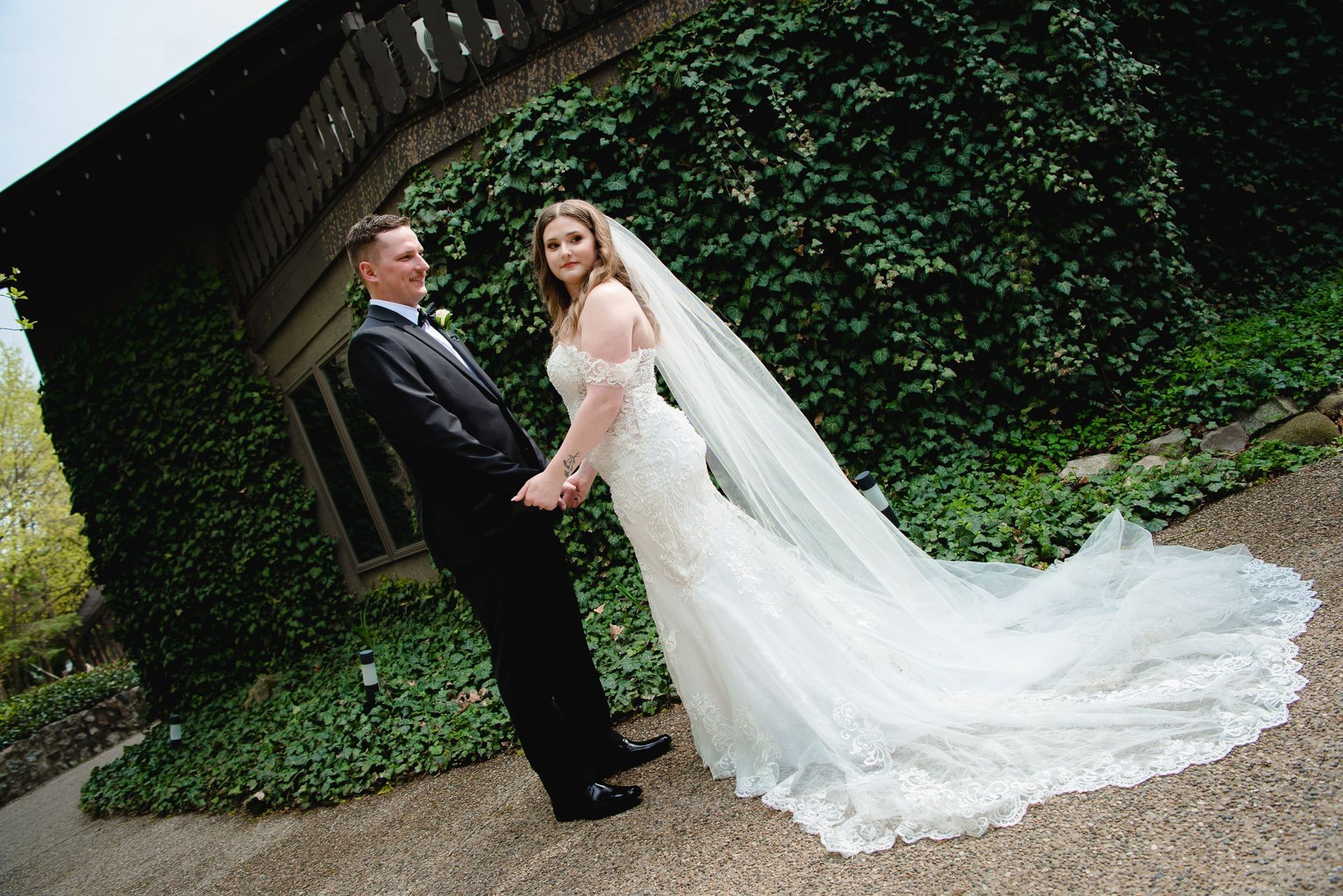A bride and groom are holding hands in front of a building covered in ivy.