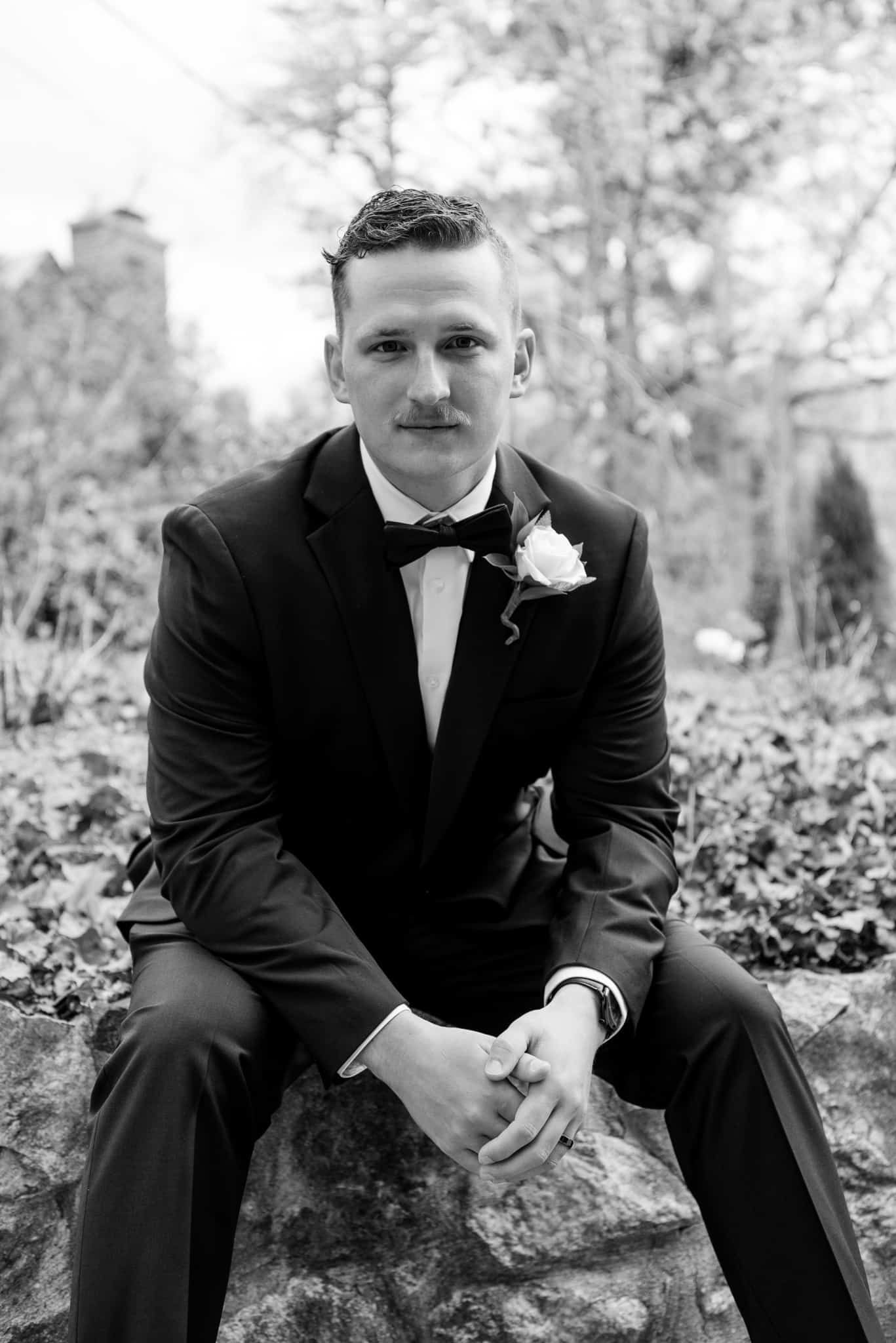 A man in a suit and bow tie is sitting on a rock.