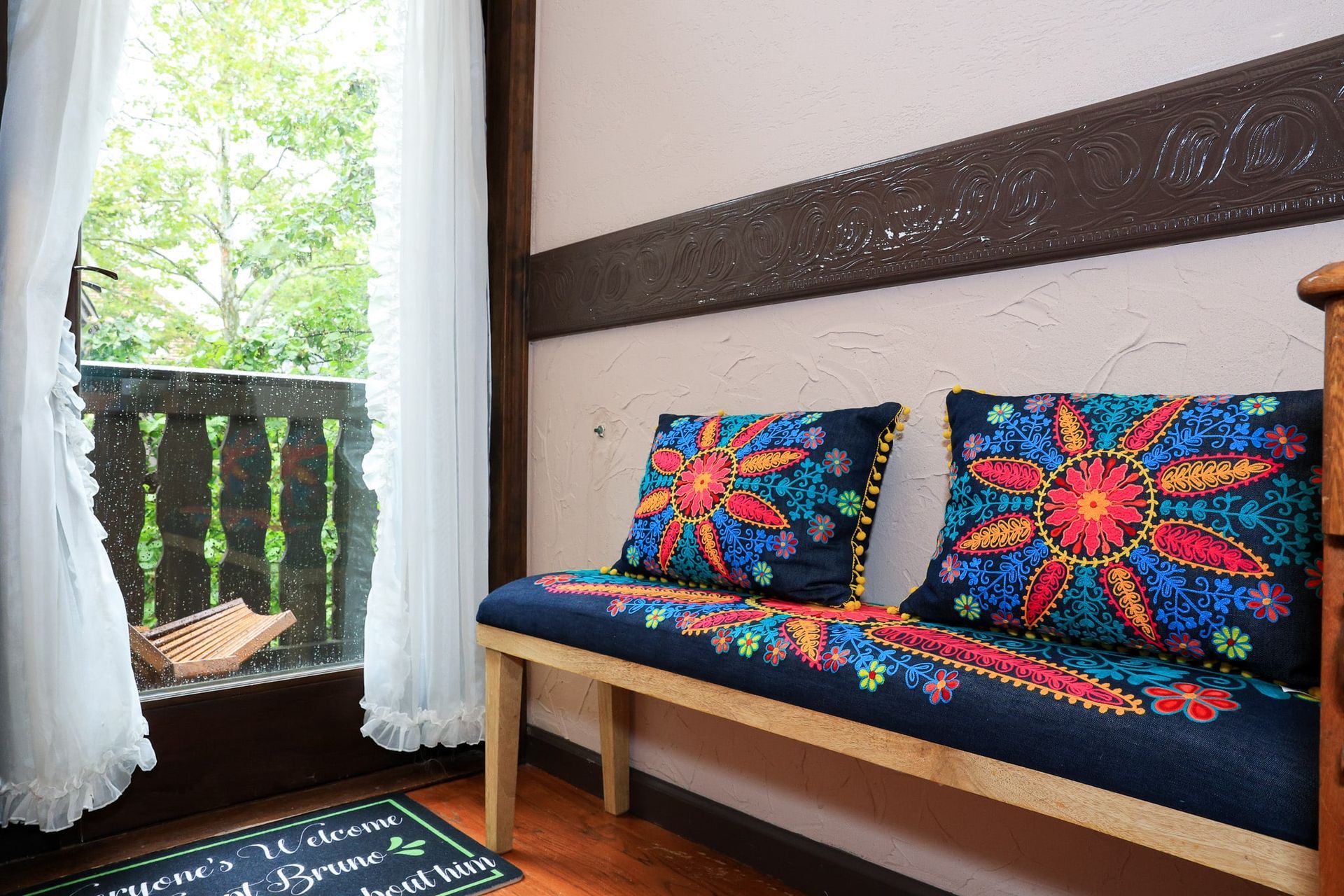 A bench with colorful pillows is sitting in front of a window.