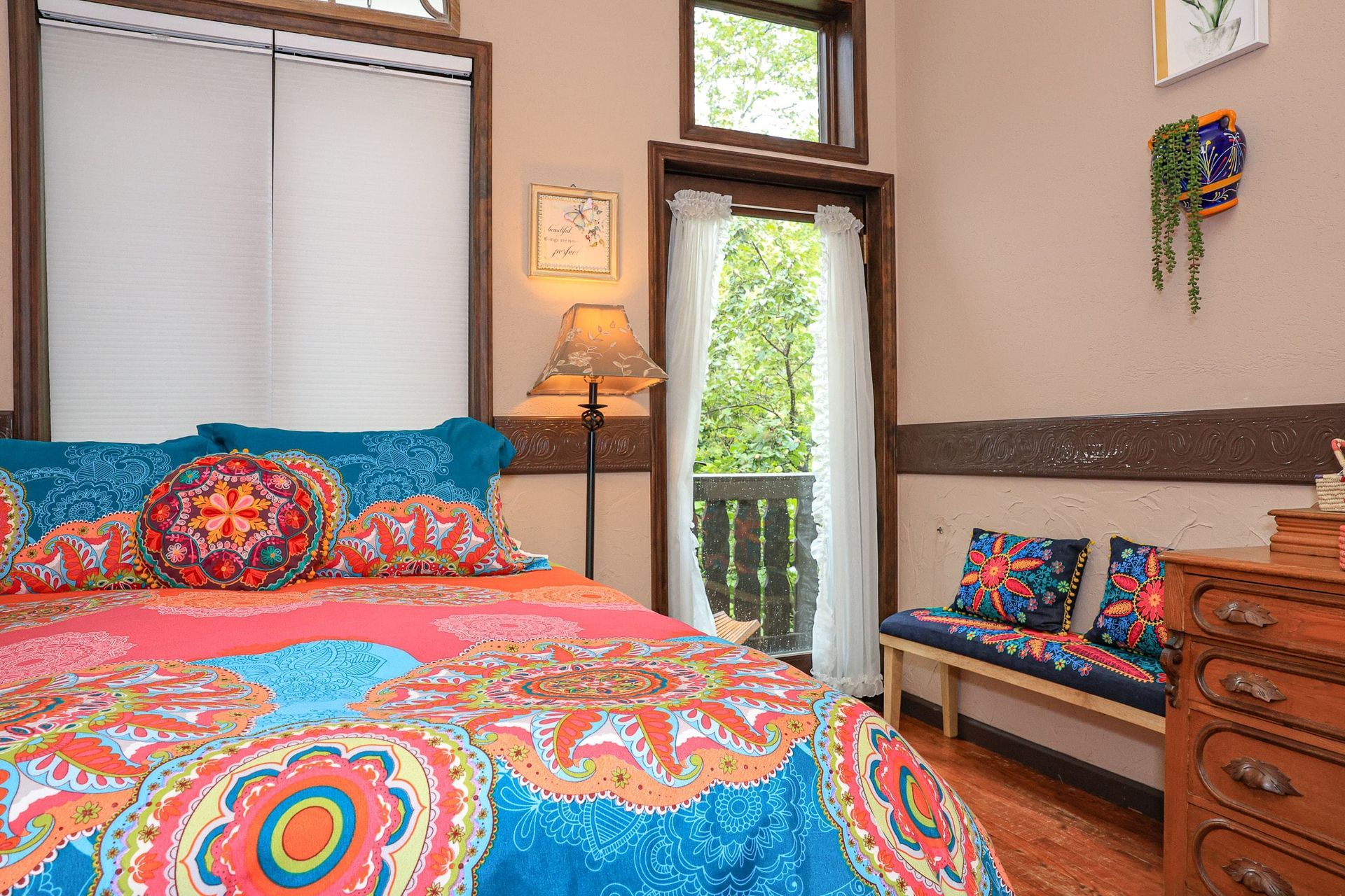 A bedroom with a bed , dresser , lamp and a balcony.