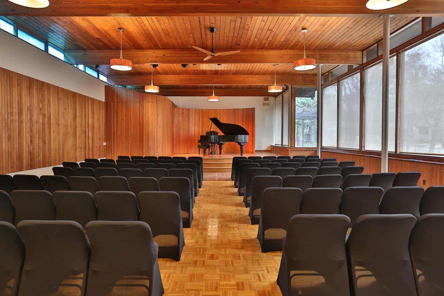 A large auditorium with rows of chairs and a piano in the background.