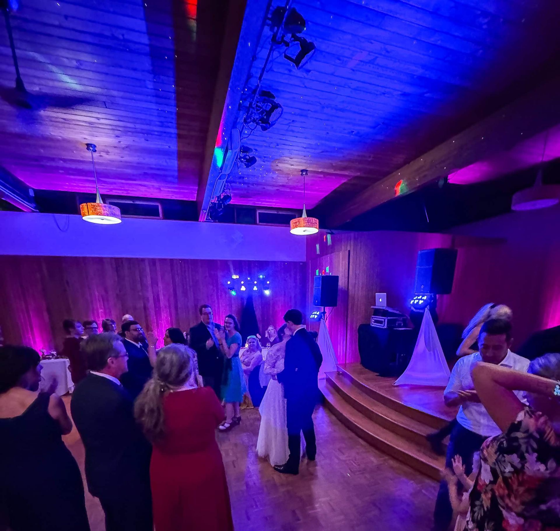 A group of people are dancing in a room with purple lights.