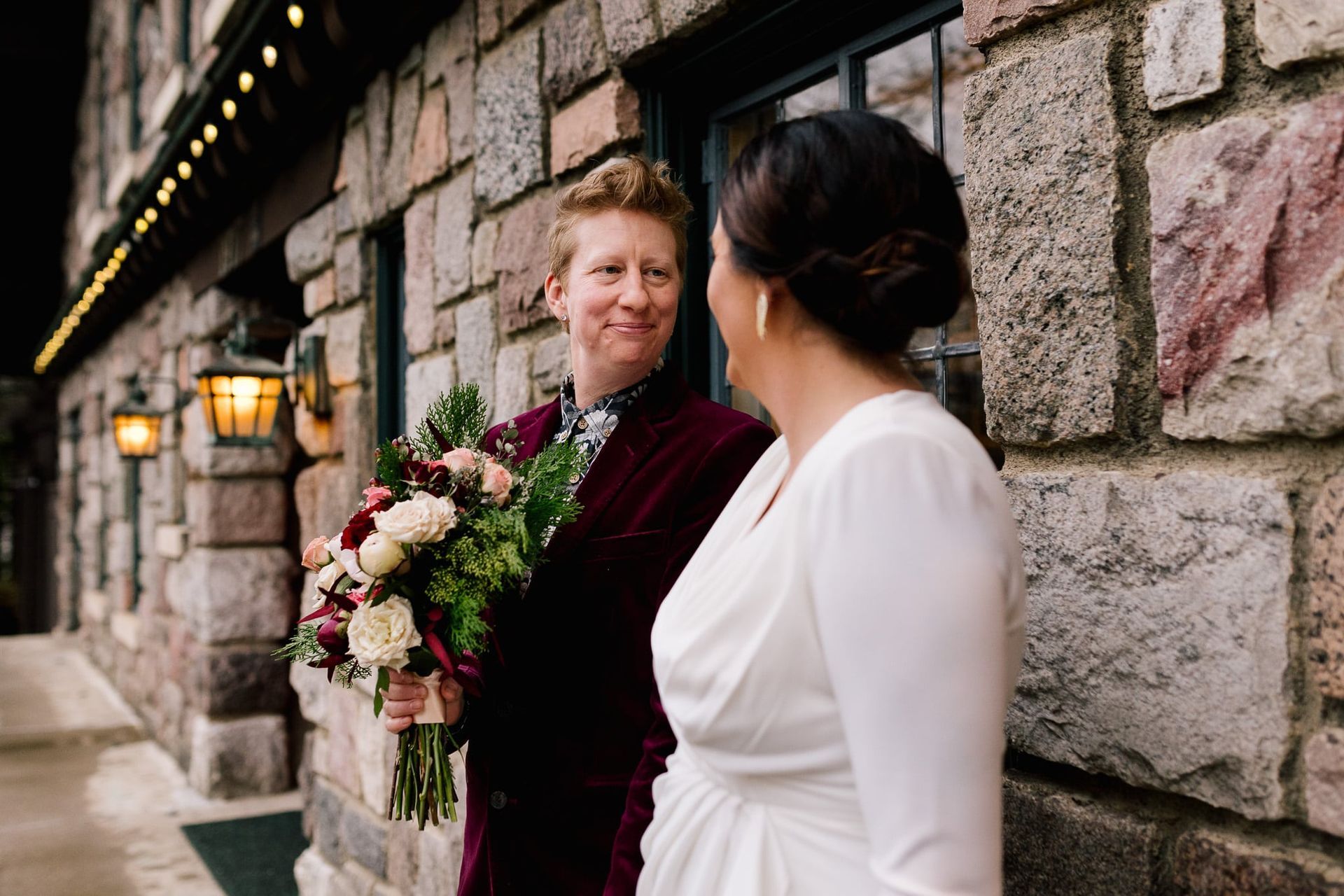 A bride and groom are standing next to each other in front of a brick building.
