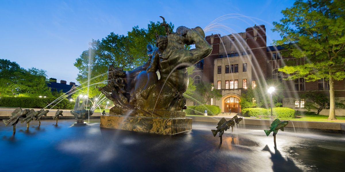 A fountain with a statue in the middle of it in front of a building.