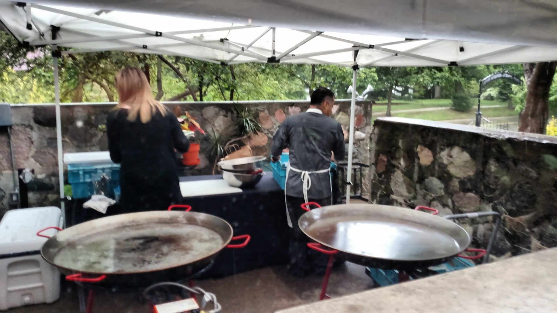 A man and a woman are cooking paella in a tent.