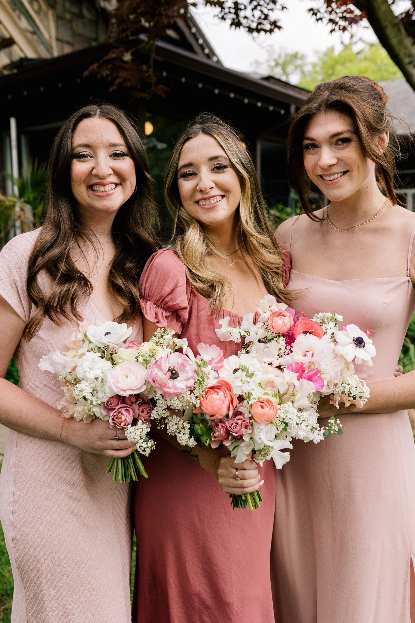 Three bridesmaids in pink dresses are posing for a picture while holding bouquets of flowers.