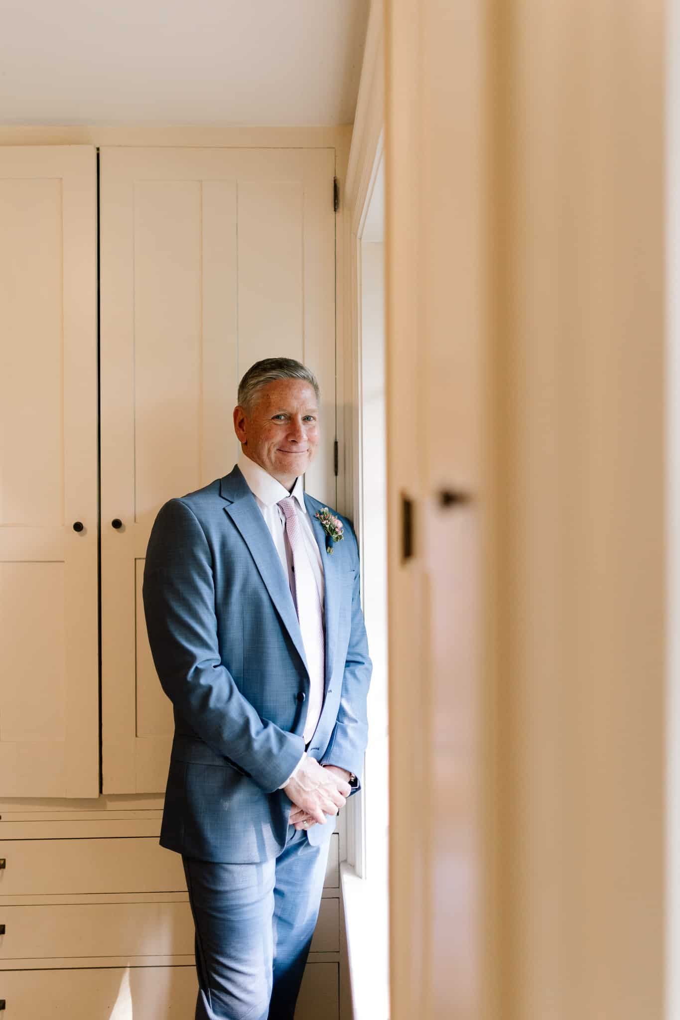 A man in a suit and tie is standing next to a window in a room.