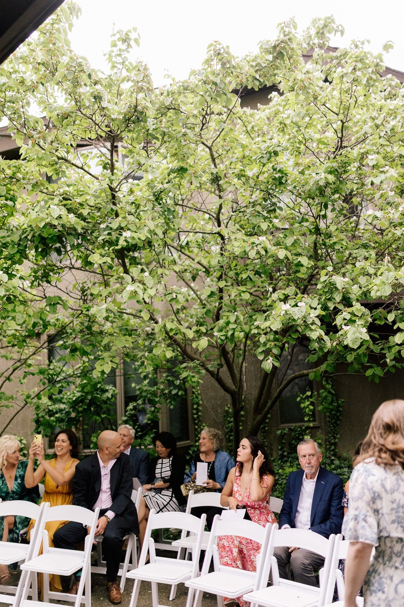 A group of people are sitting in white chairs at a wedding ceremony.