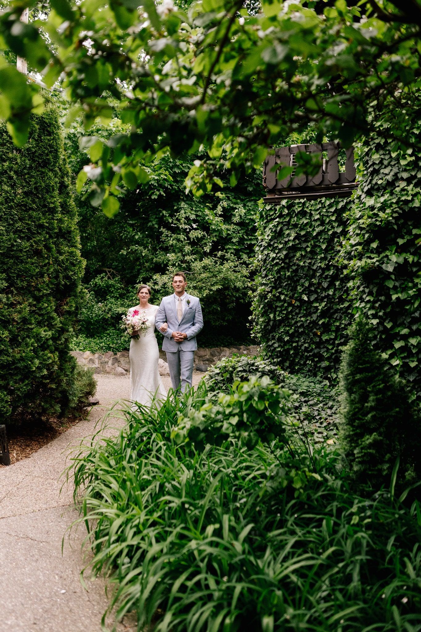 A bride and groom are walking down a path in a garden.