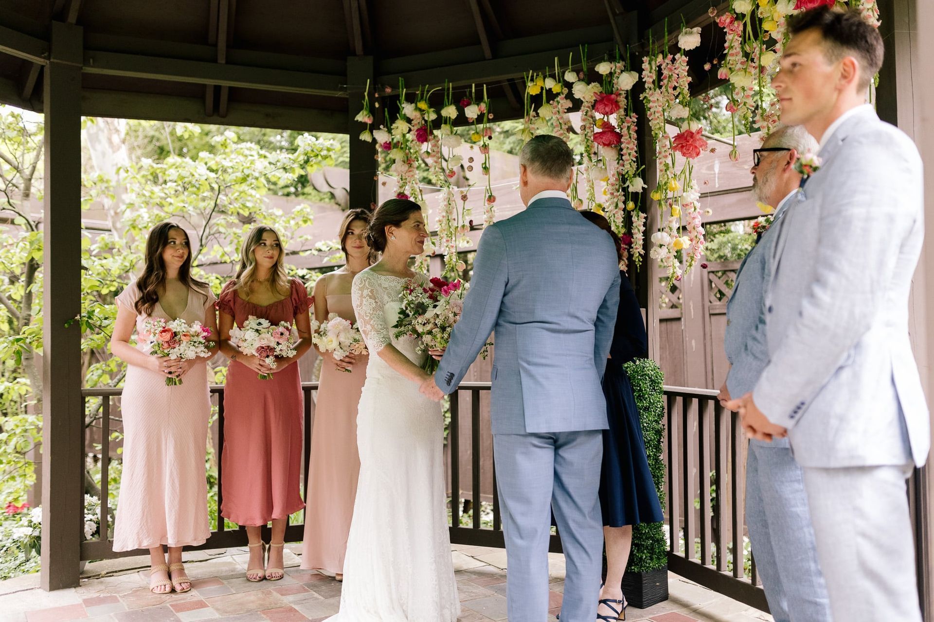 A bride and groom are holding hands during their wedding ceremony in a gazebo.