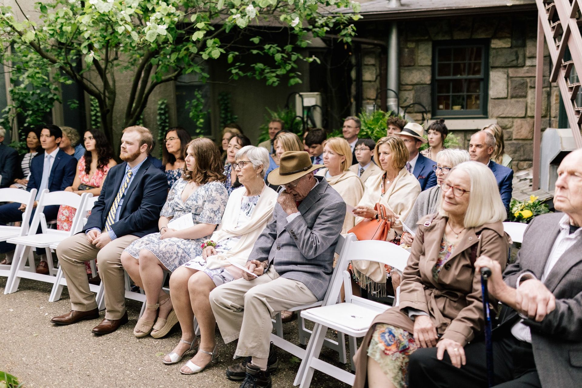 A large group of people are sitting in white chairs watching a wedding ceremony.