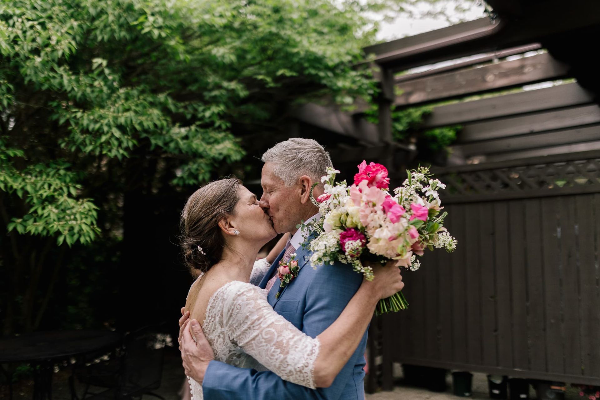 A bride and groom kissing while holding a bouquet of flowers.