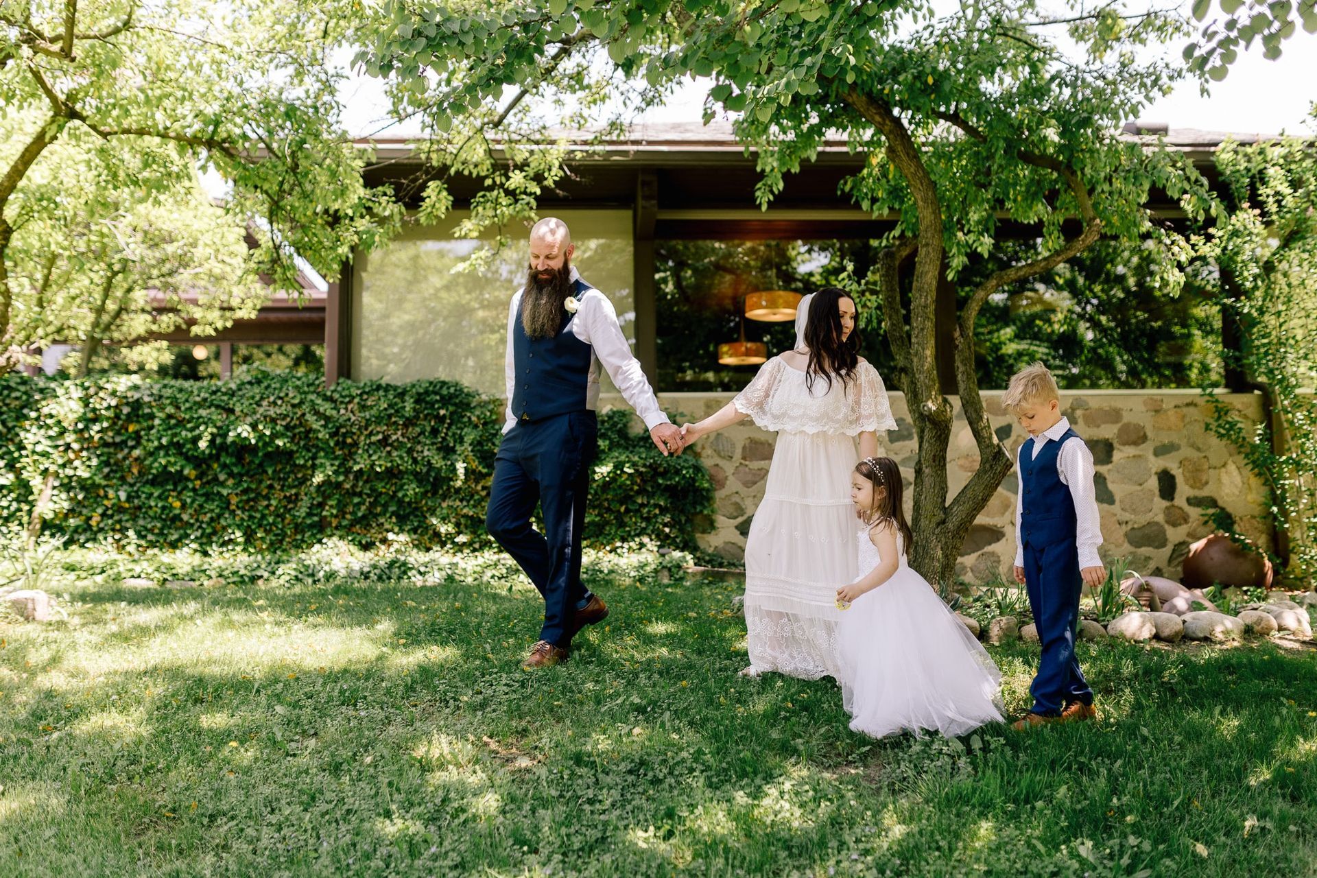 A bride and groom are holding hands with their children in front of a house.