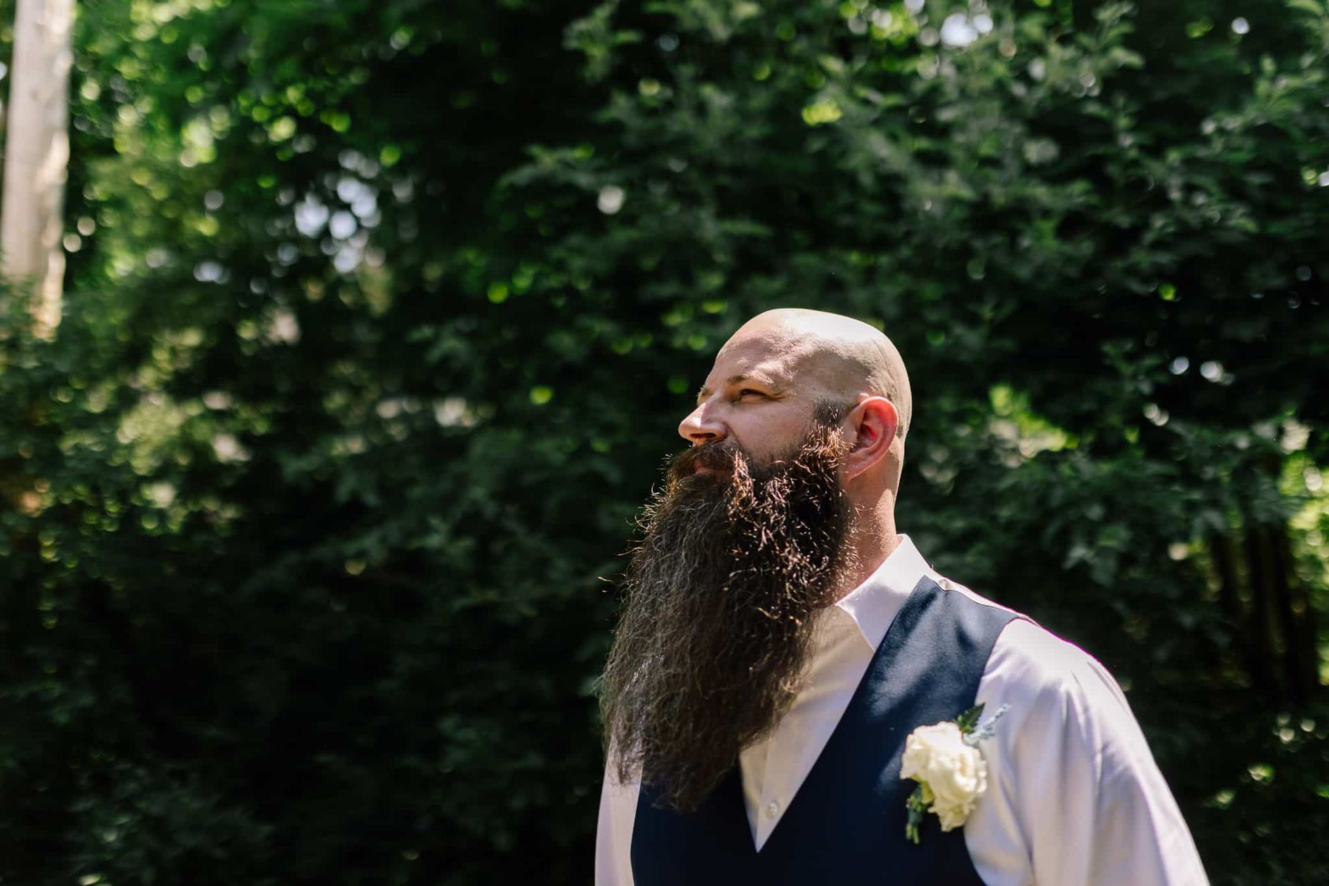 A man with a long beard is standing in front of trees.