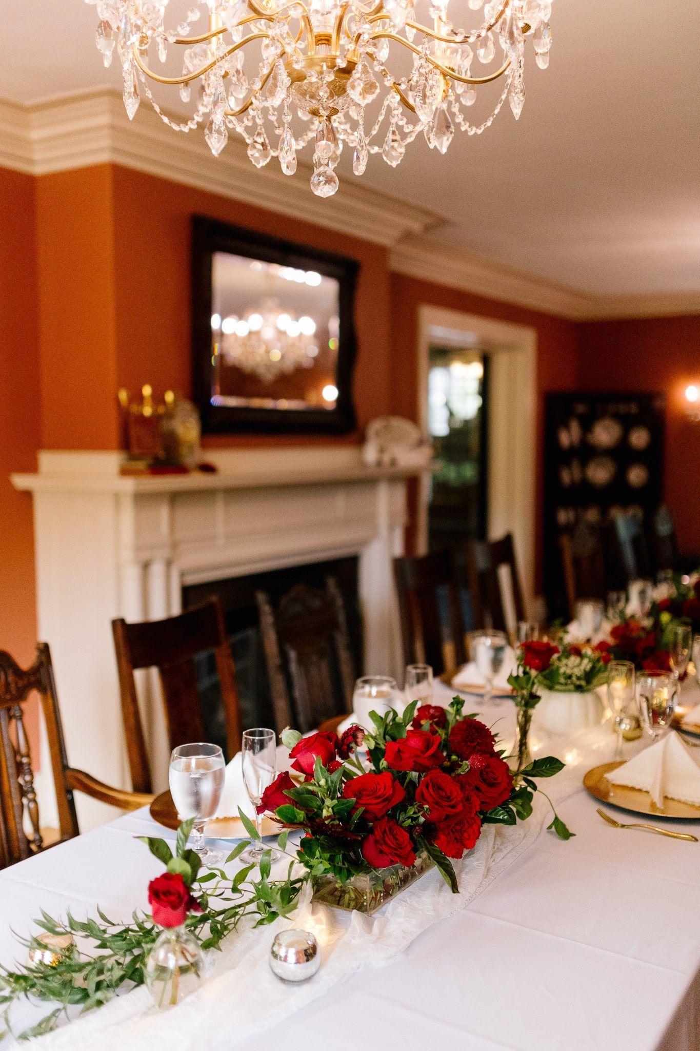 A long table with red roses and candles on it in a dining room.