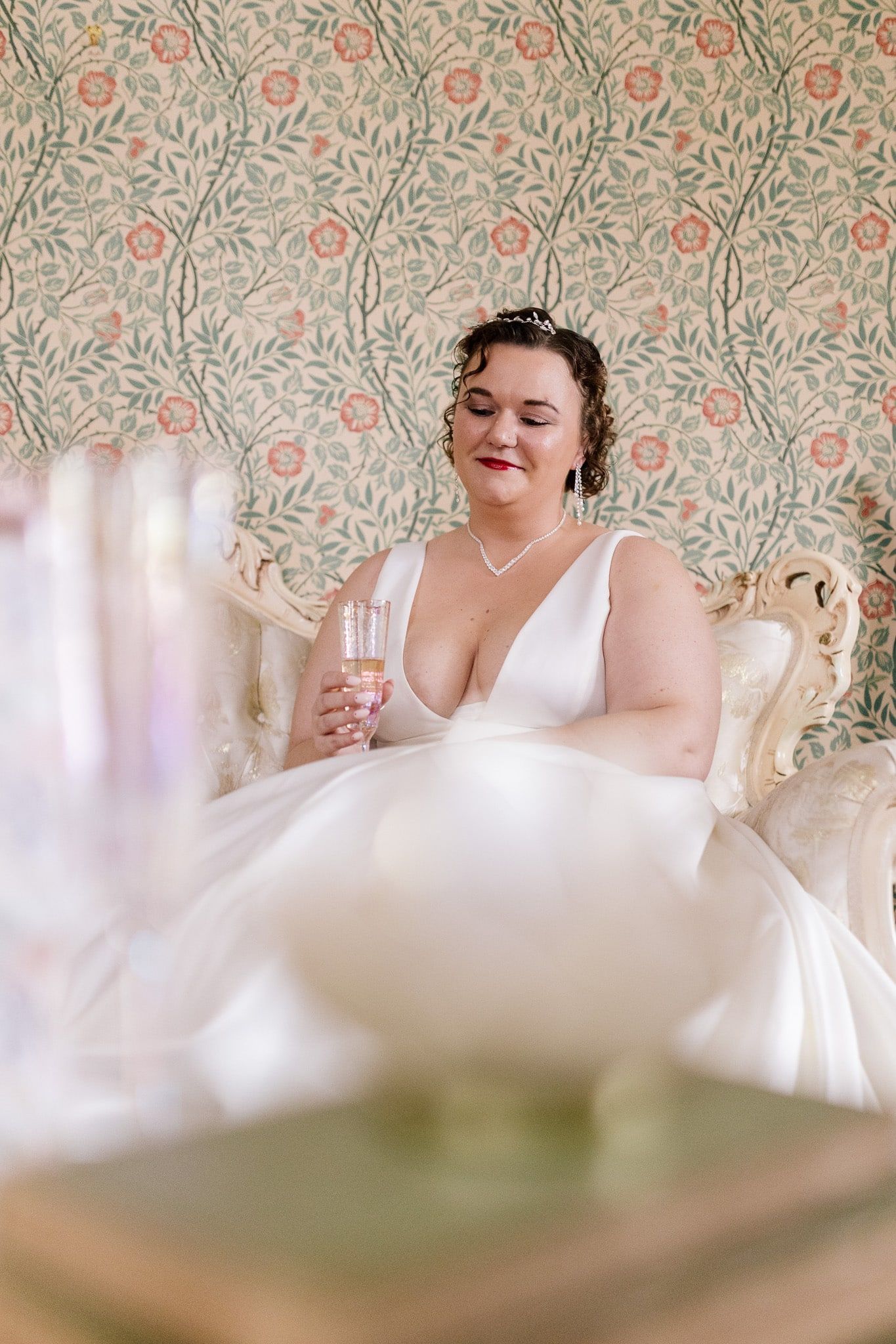 A woman in a wedding dress is sitting on a couch holding a glass of wine.