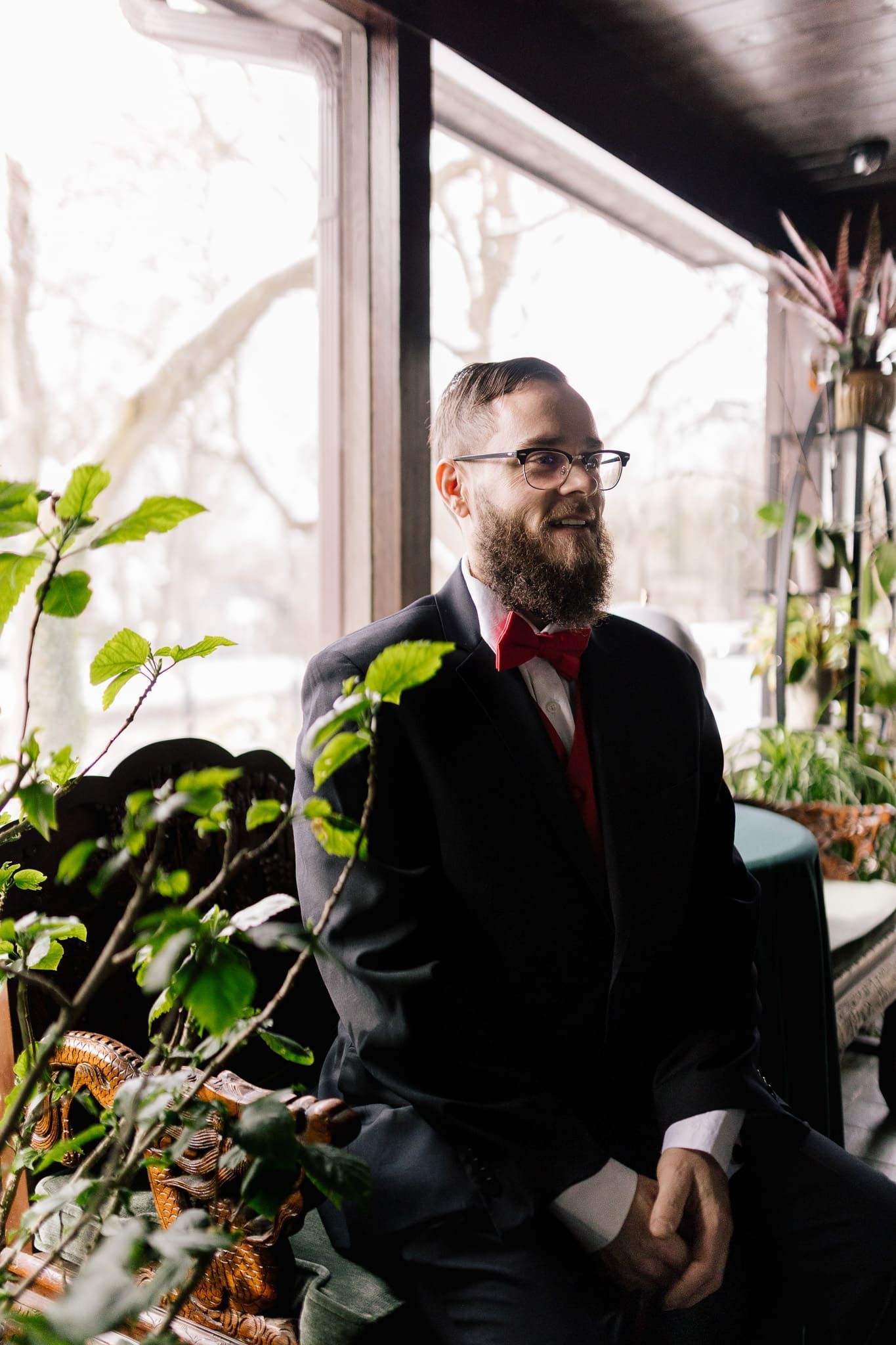 A man in a suit and bow tie is sitting in front of a window.