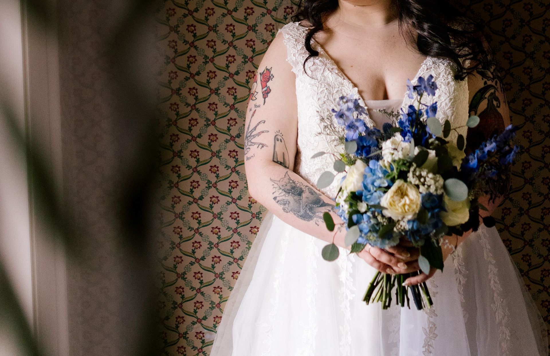 A bride with tattoos on her arms is holding a bouquet of flowers.