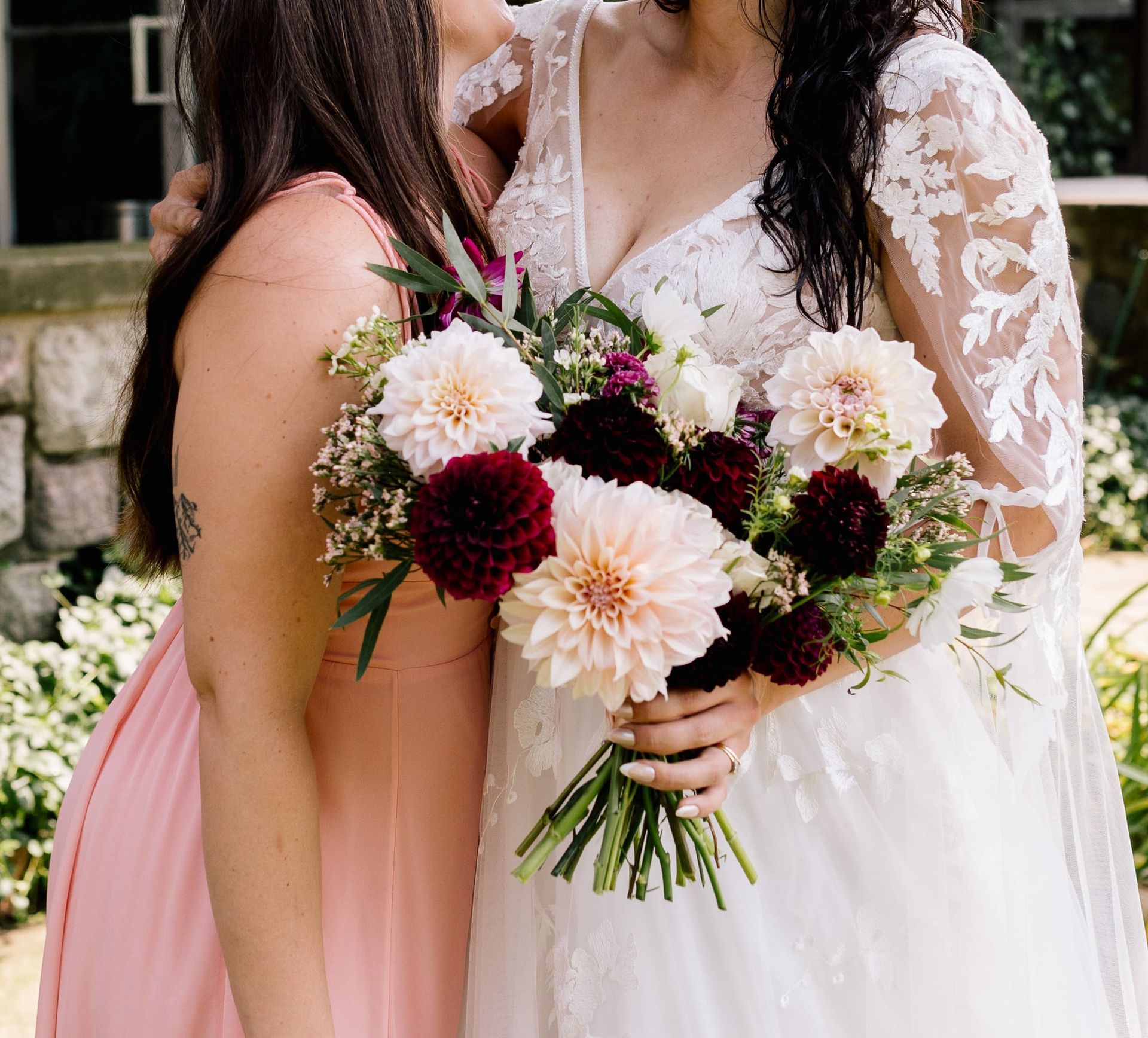 A bride and her bridesmaid are posing for a picture while the bride is holding a bouquet of flowers.