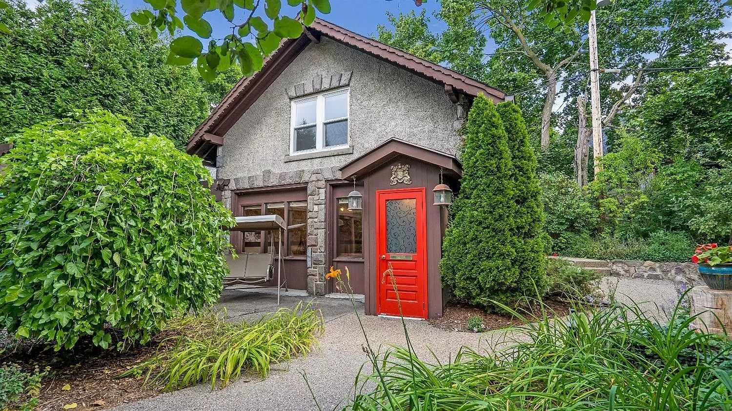 A small house with a red door is surrounded by trees and bushes.
