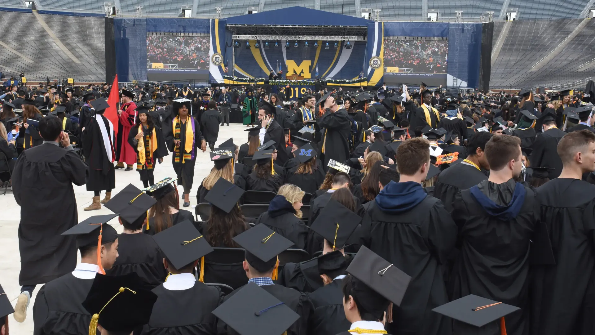 A large group of graduates are standing in a stadium.