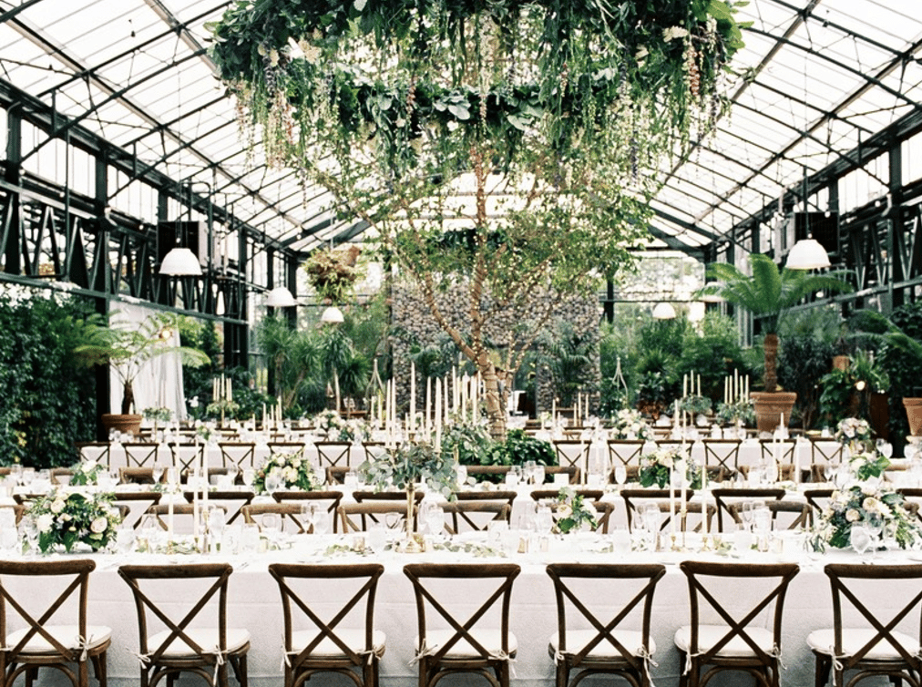 A large greenhouse with tables and chairs and a chandelier hanging from the ceiling.