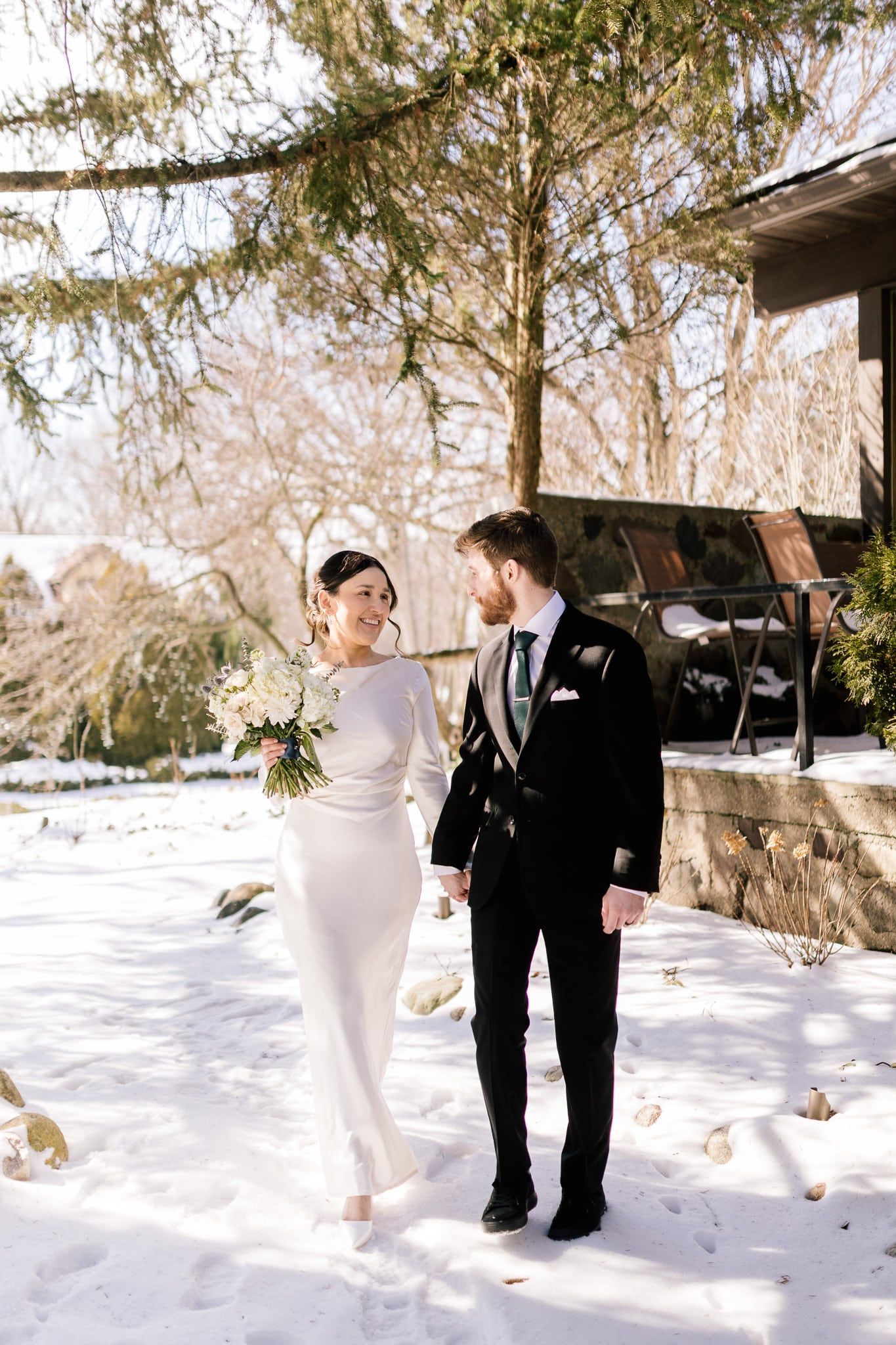 A bride and groom are walking in the snow holding hands.