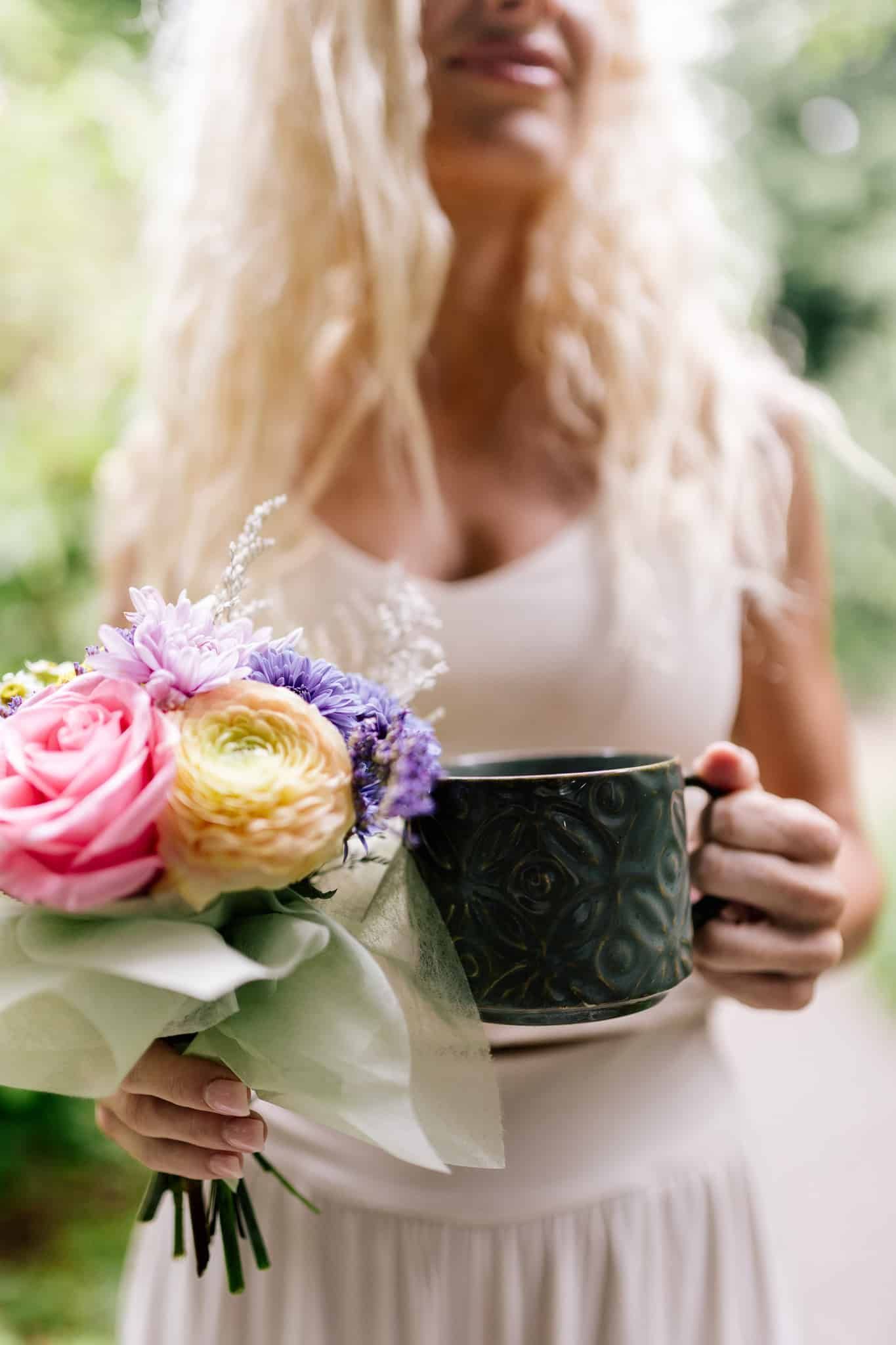 A woman is holding a bouquet of flowers and a cup of coffee.