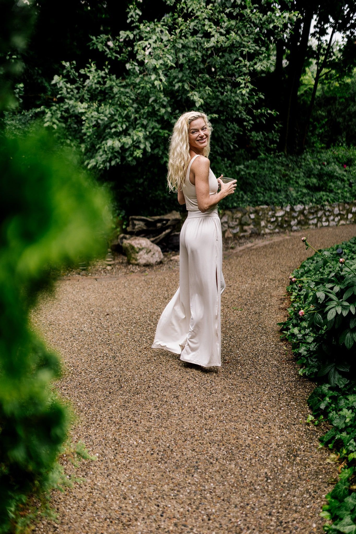 A woman in a white dress is standing on a gravel path in a garden.