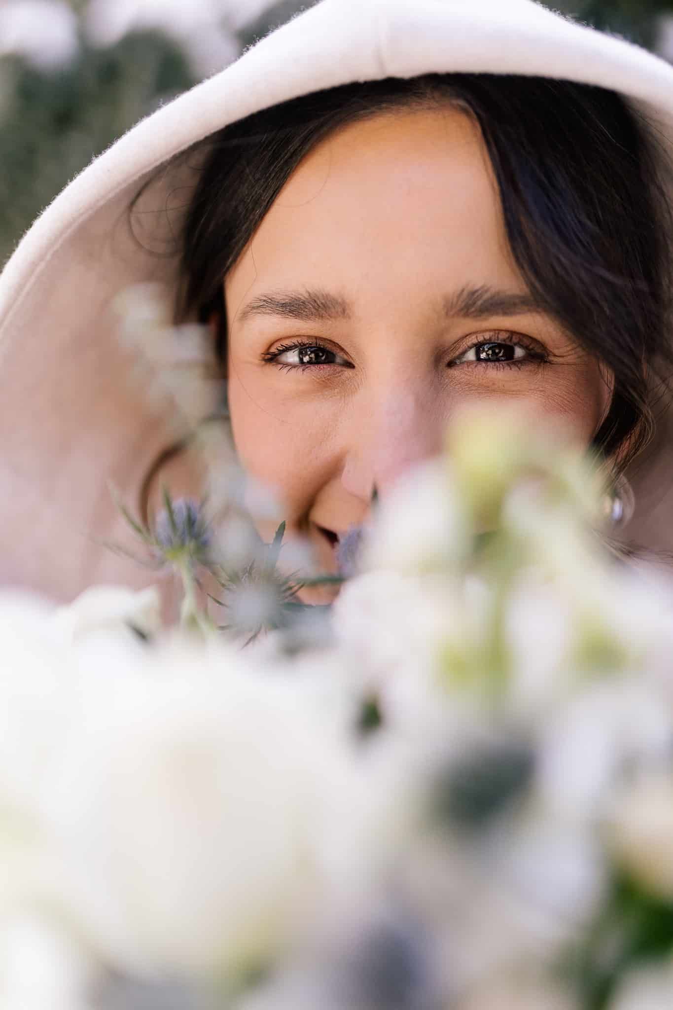 A woman wearing a hat is peeking out from behind a bouquet of white flowers.