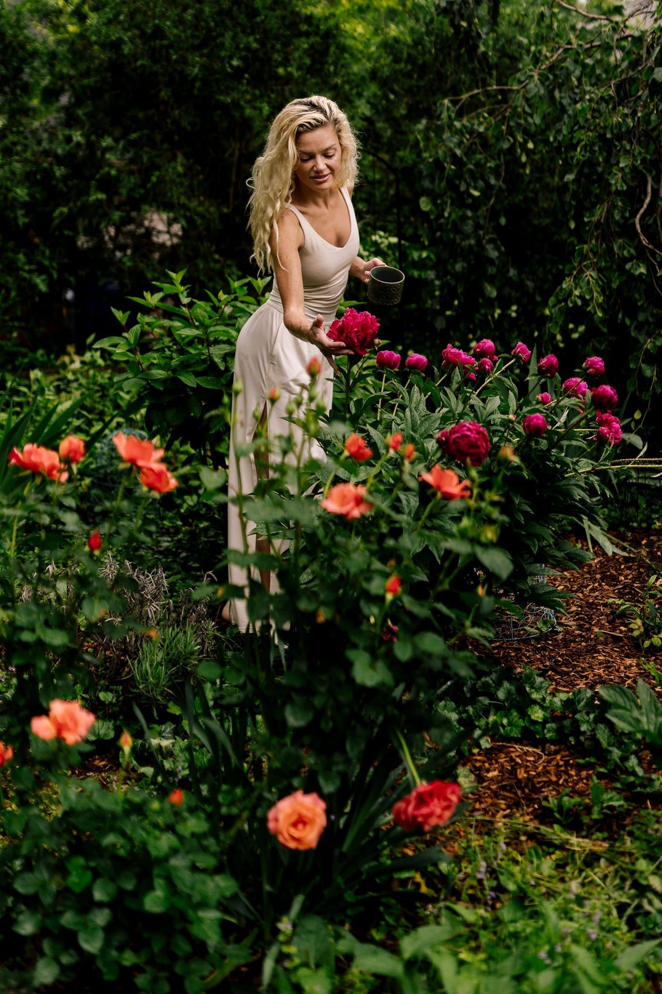 A woman in a white dress is standing in a garden surrounded by flowers.