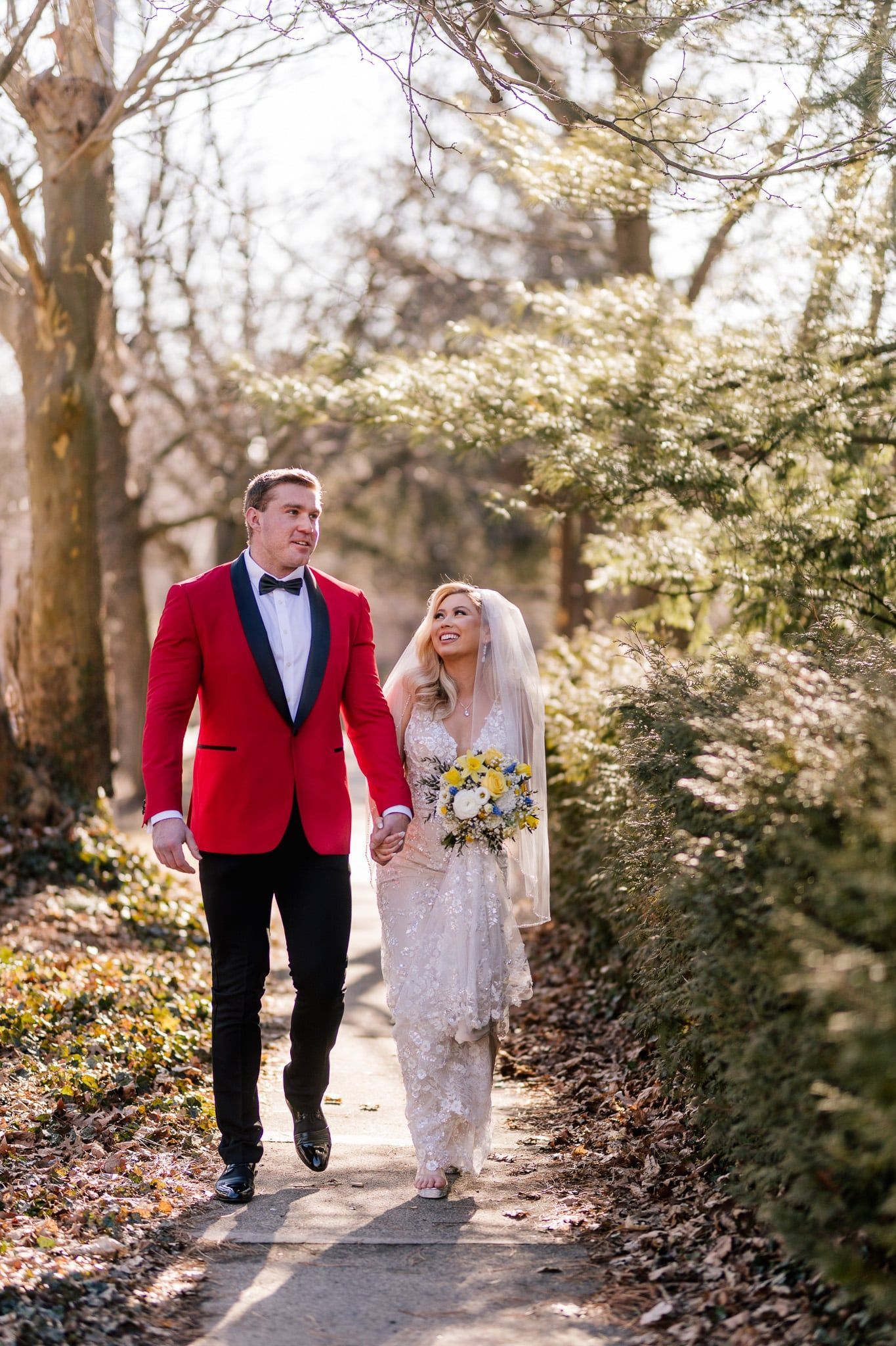A bride and groom are walking down a path in the woods holding hands.
