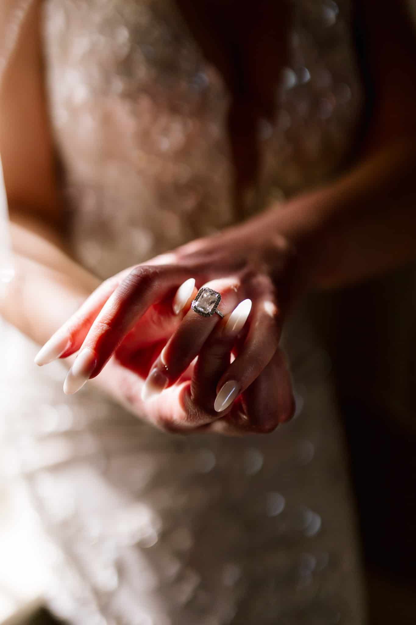 A woman in a wedding dress is holding a diamond ring on her finger.