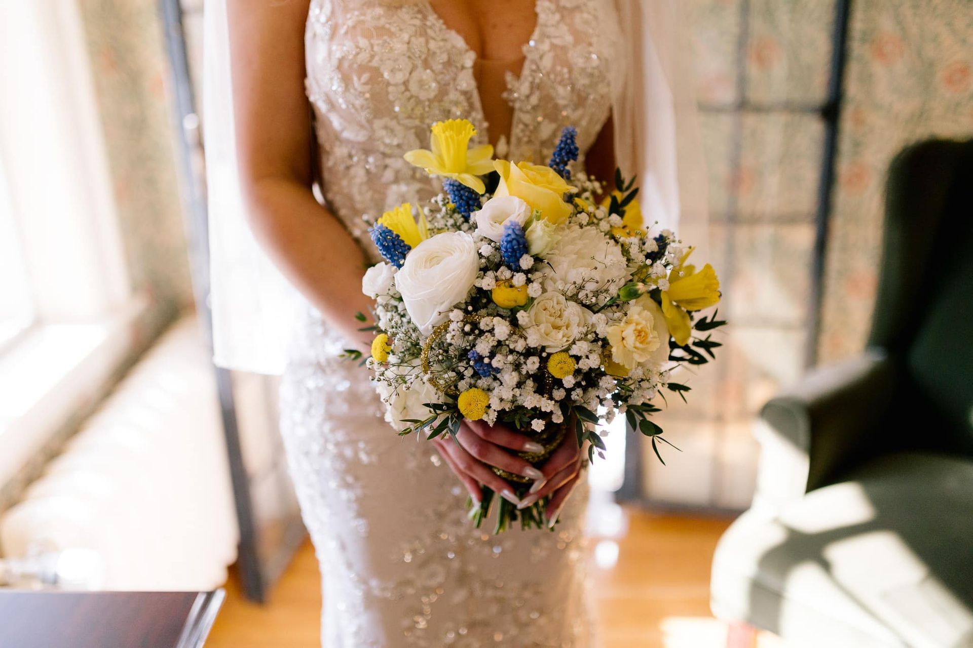 A bride in a wedding dress is holding a bouquet of yellow and blue flowers.