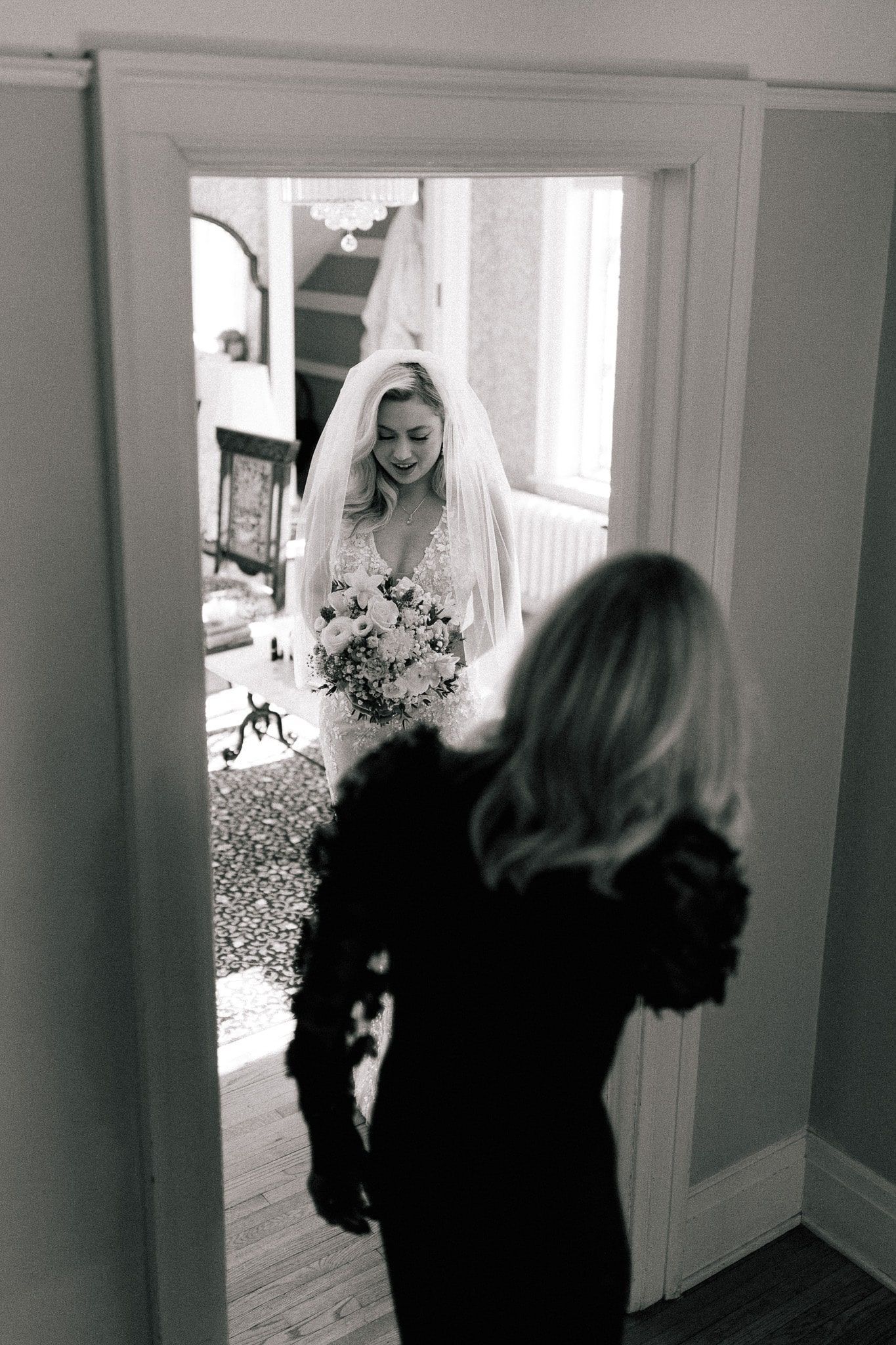 A black and white photo of a bride in a veil standing in a doorway.