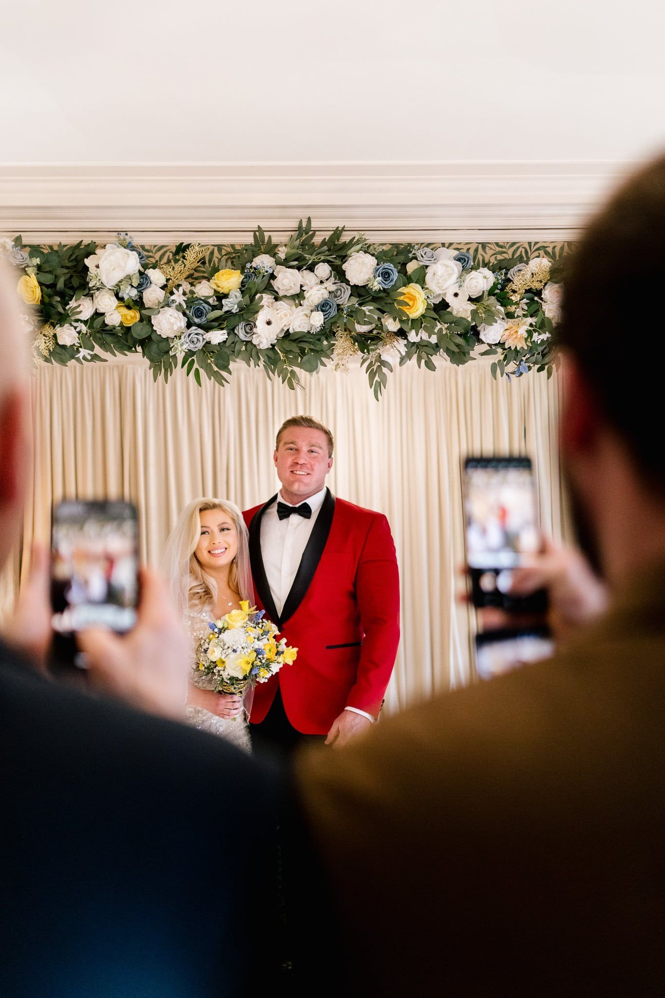 A man in a red suit is taking a picture of a bride and groom.
