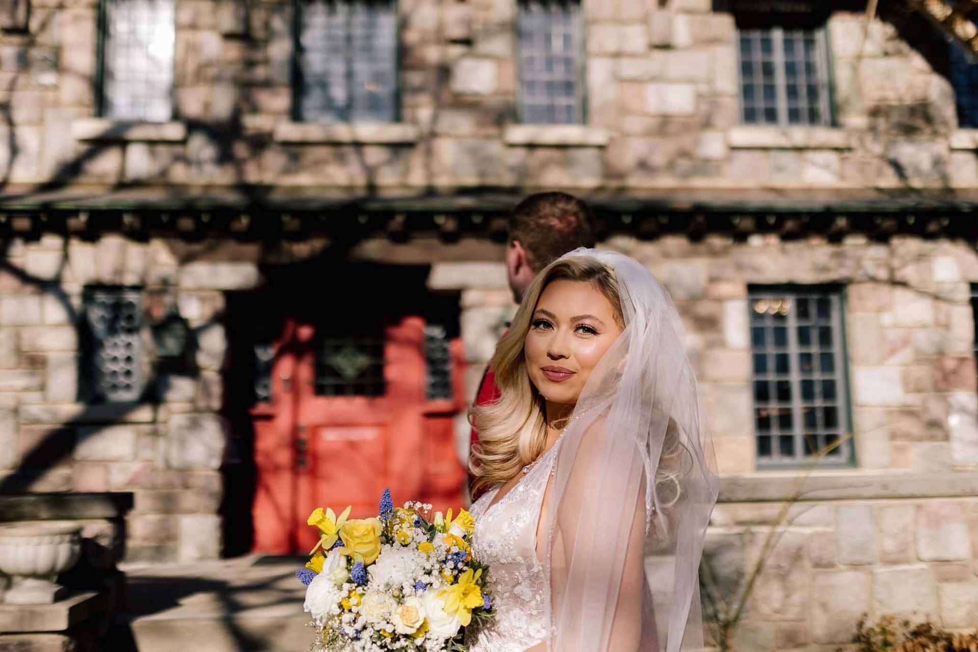A bride is holding a bouquet of flowers in front of a stone building.
