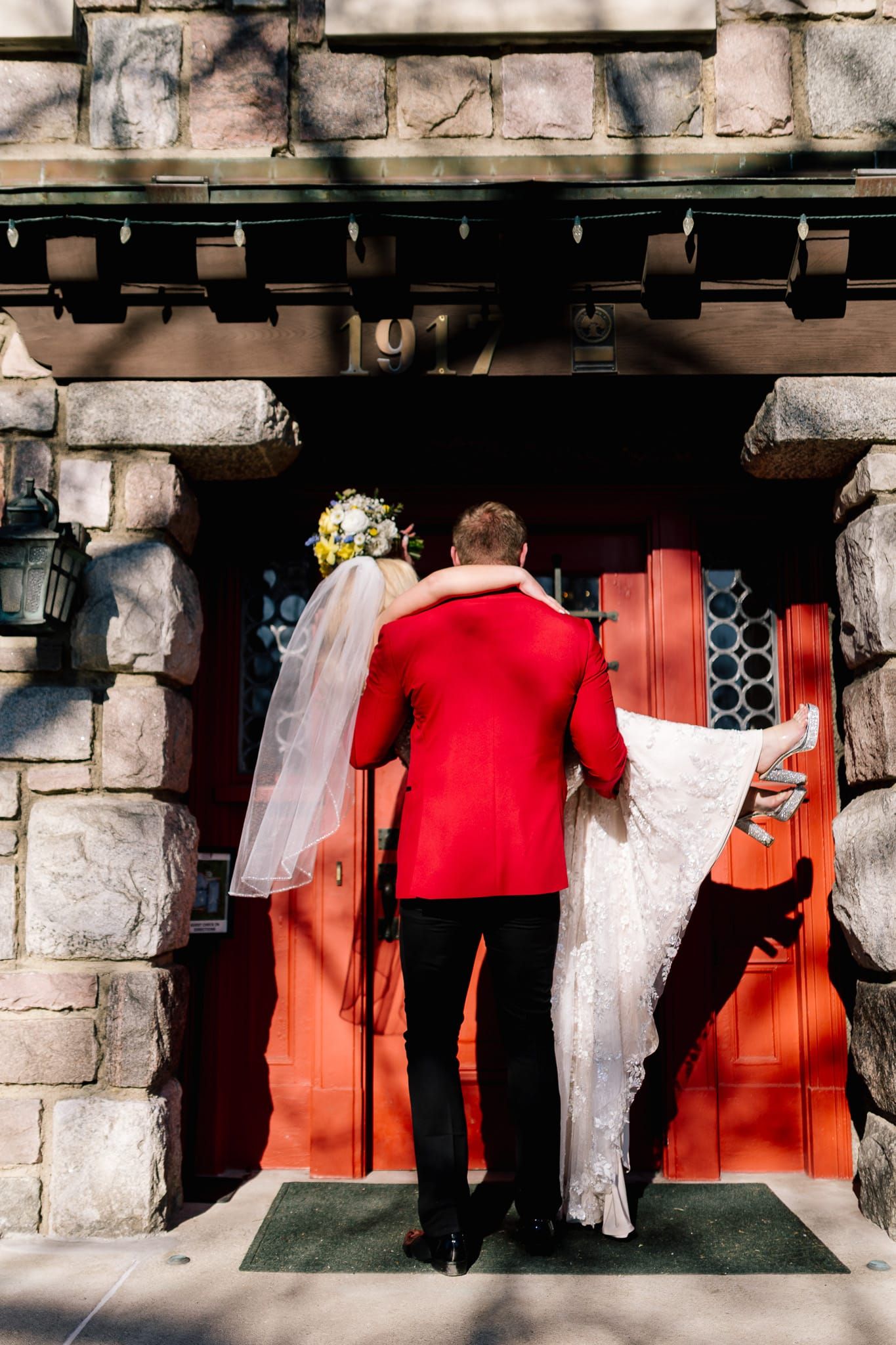 A bride and groom are standing in front of a red door.